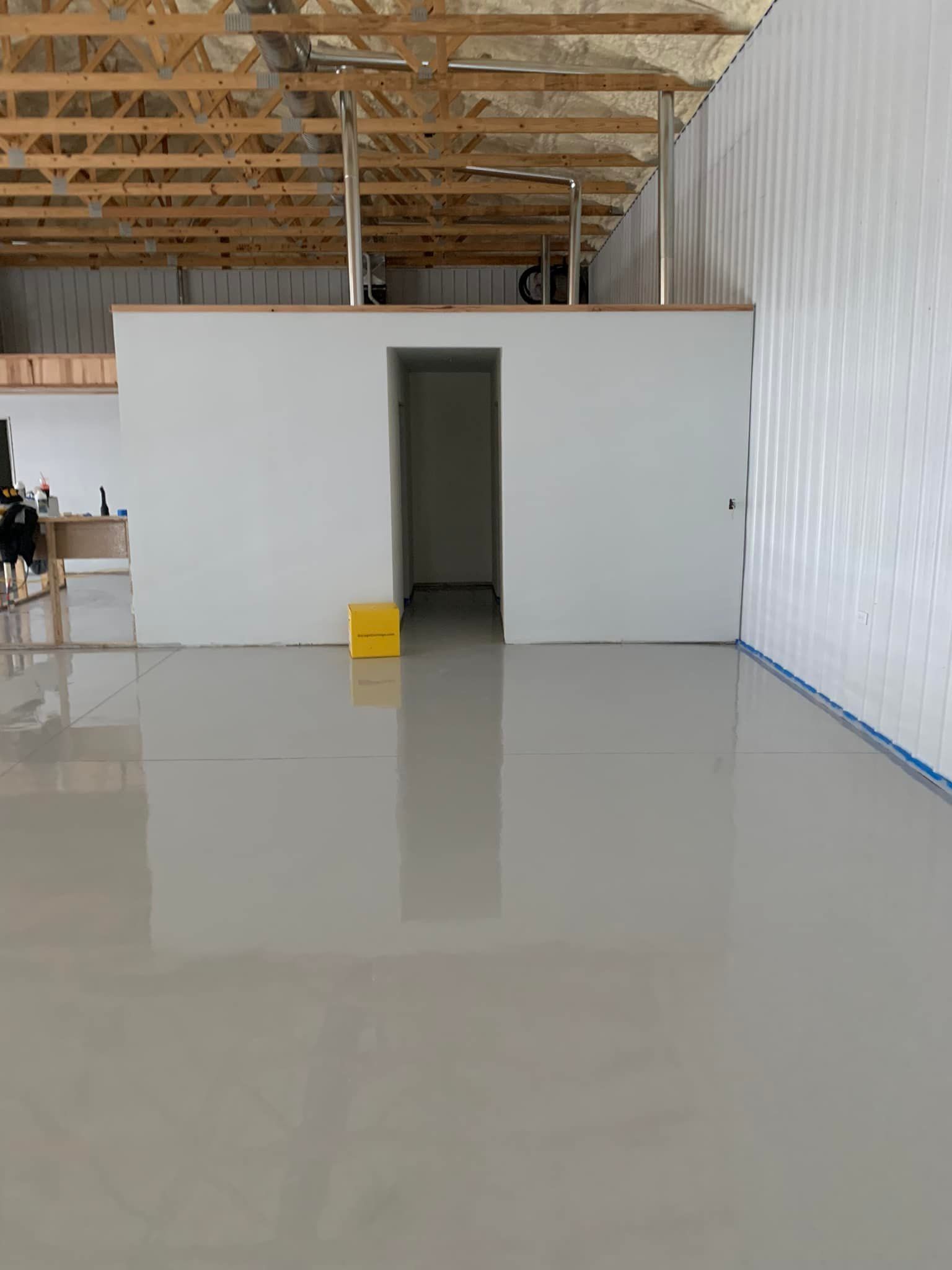 Empty industrial room with glossy floor, white walls, exposed ceiling beams, and a doorway in the back wall