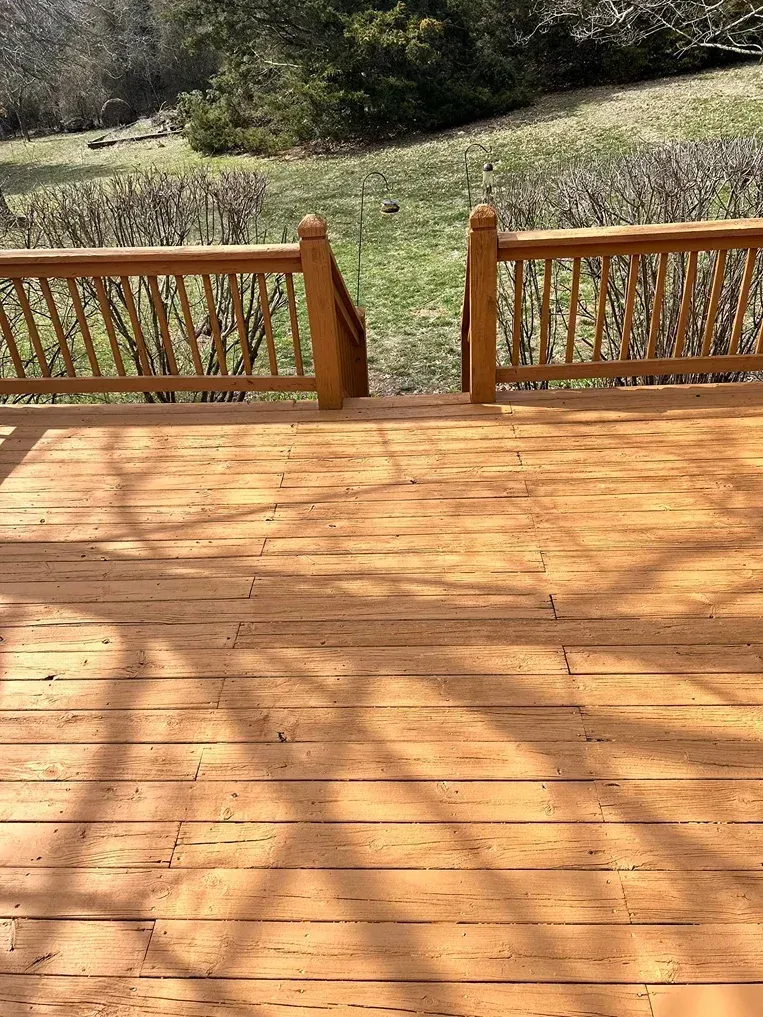 Wooden deck with railing and open gate overlooking a grassy yard and shrubs in sunlight