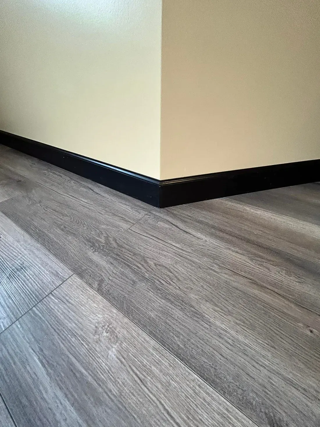 Corner of a room with beige walls, black baseboard, and gray wood-look flooring