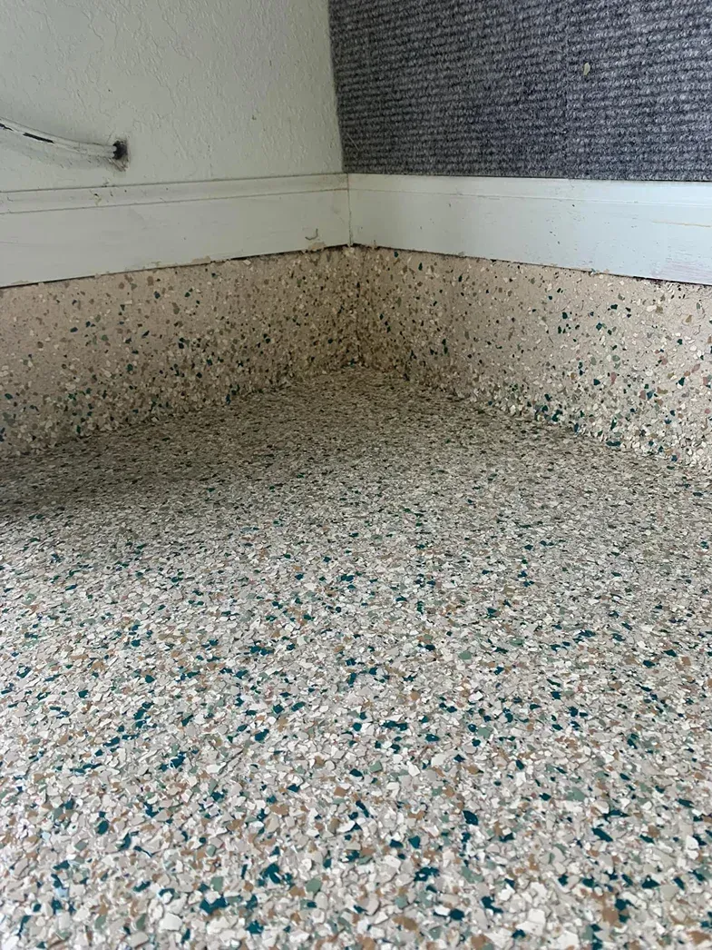 Speckled terrazzo floor and curved white wall corner with a small outlet and cable on the left