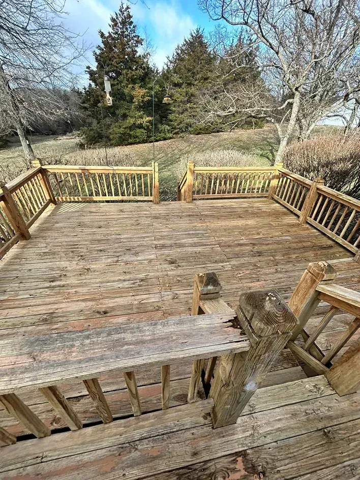 Wooden deck overlooking a grassy yard with trees and a railing, seen from the steps.