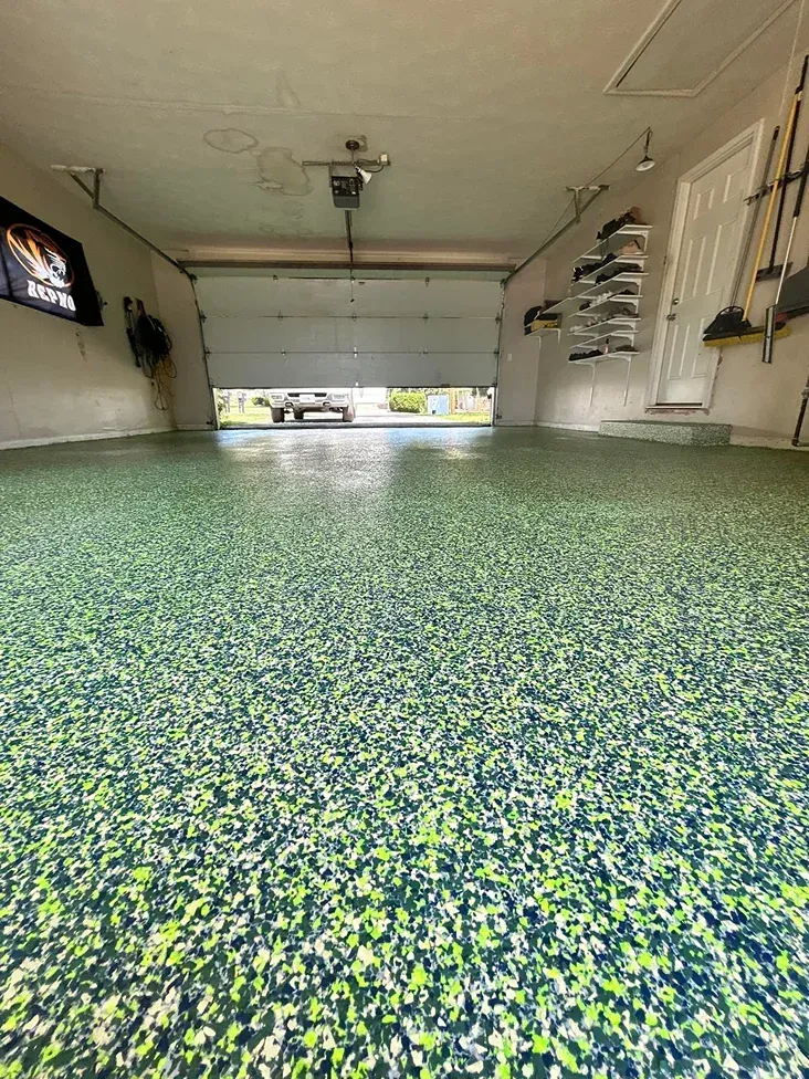 Garage interior with speckled epoxy floor, white walls, and an open garage door at the far end.