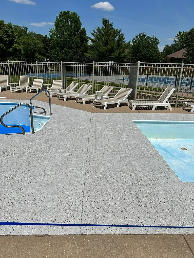 Poolside lounge chairs beside a swimming pool under a sunny blue sky.