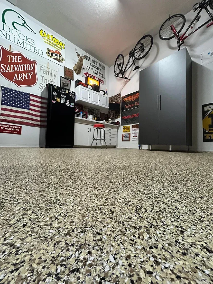 Garage interior with speckled floor, wall-mounted bikes, gray cabinets, and an American flag poster.