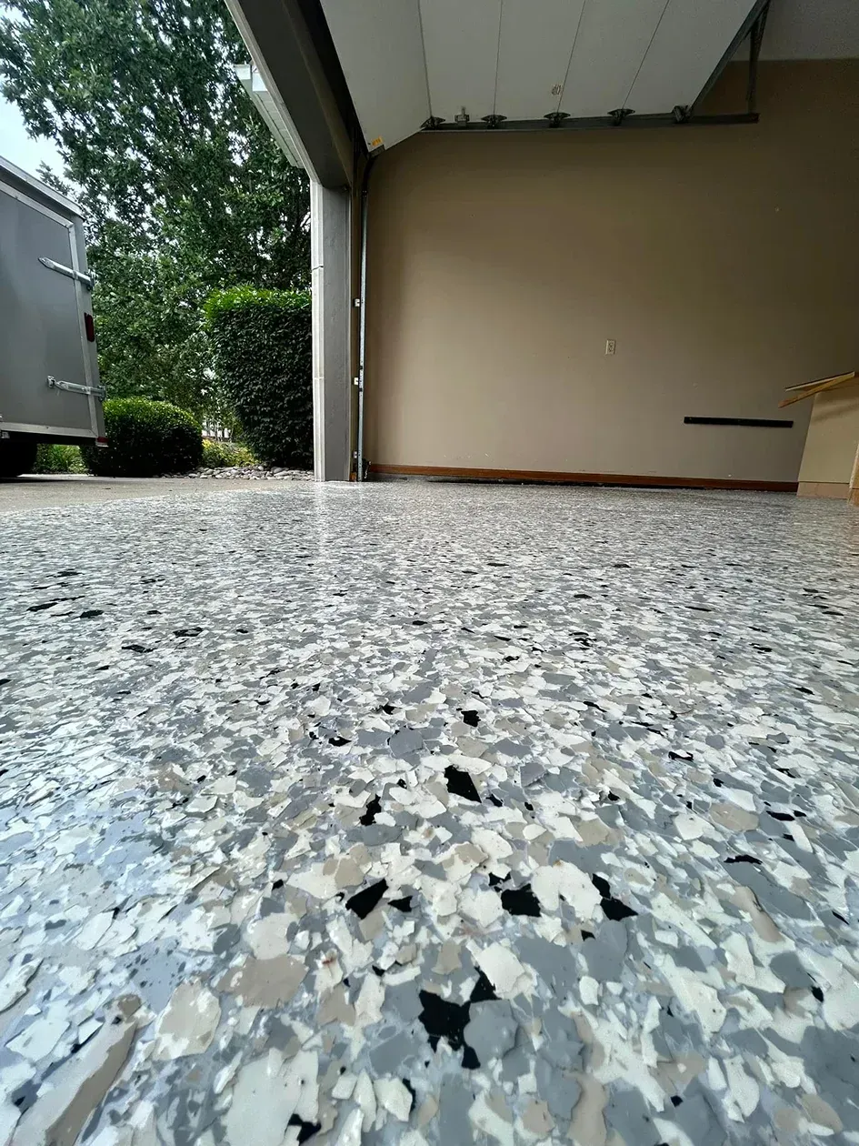 Low-angle view of a speckled concrete garage floor with an open doorway and beige wall.