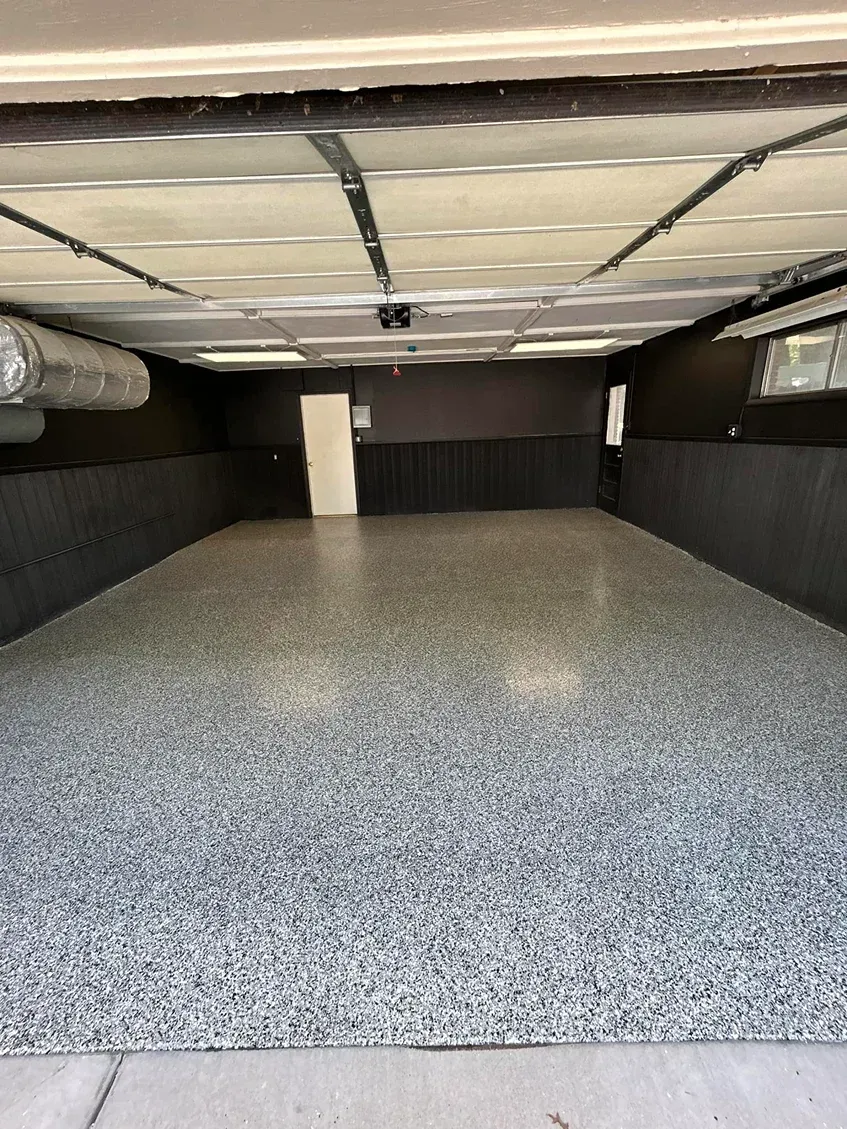 Empty indoor garage with gray epoxy floor, white ceiling, and dark walls.