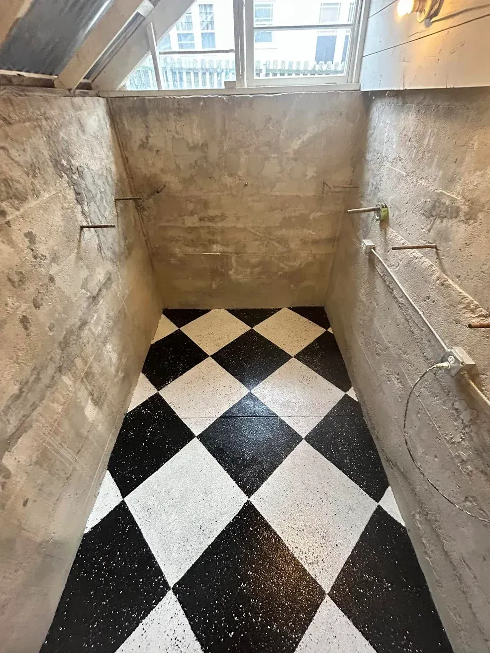 Narrow stone stairwell with black-and-white checkered tile floor and a small window at the top.