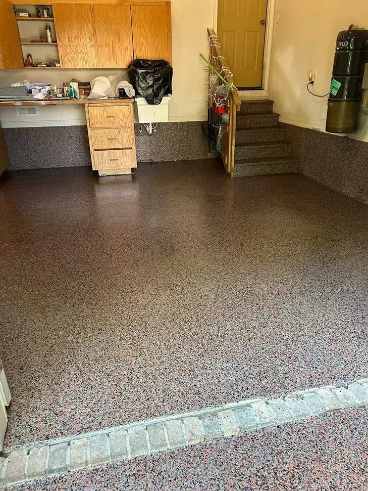 Empty indoor room with speckled floor, wood cabinets, and stairs leading up on the right
