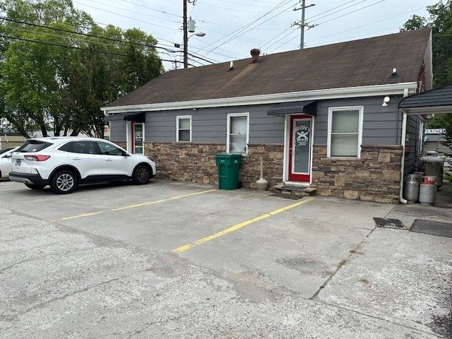 Small gray building with stone front, red door, white SUV parked in front, and empty parking lot.
