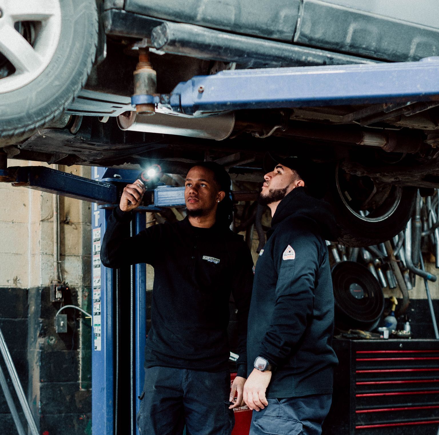 Deux hommes travaillent sous une voiture dans un garage.