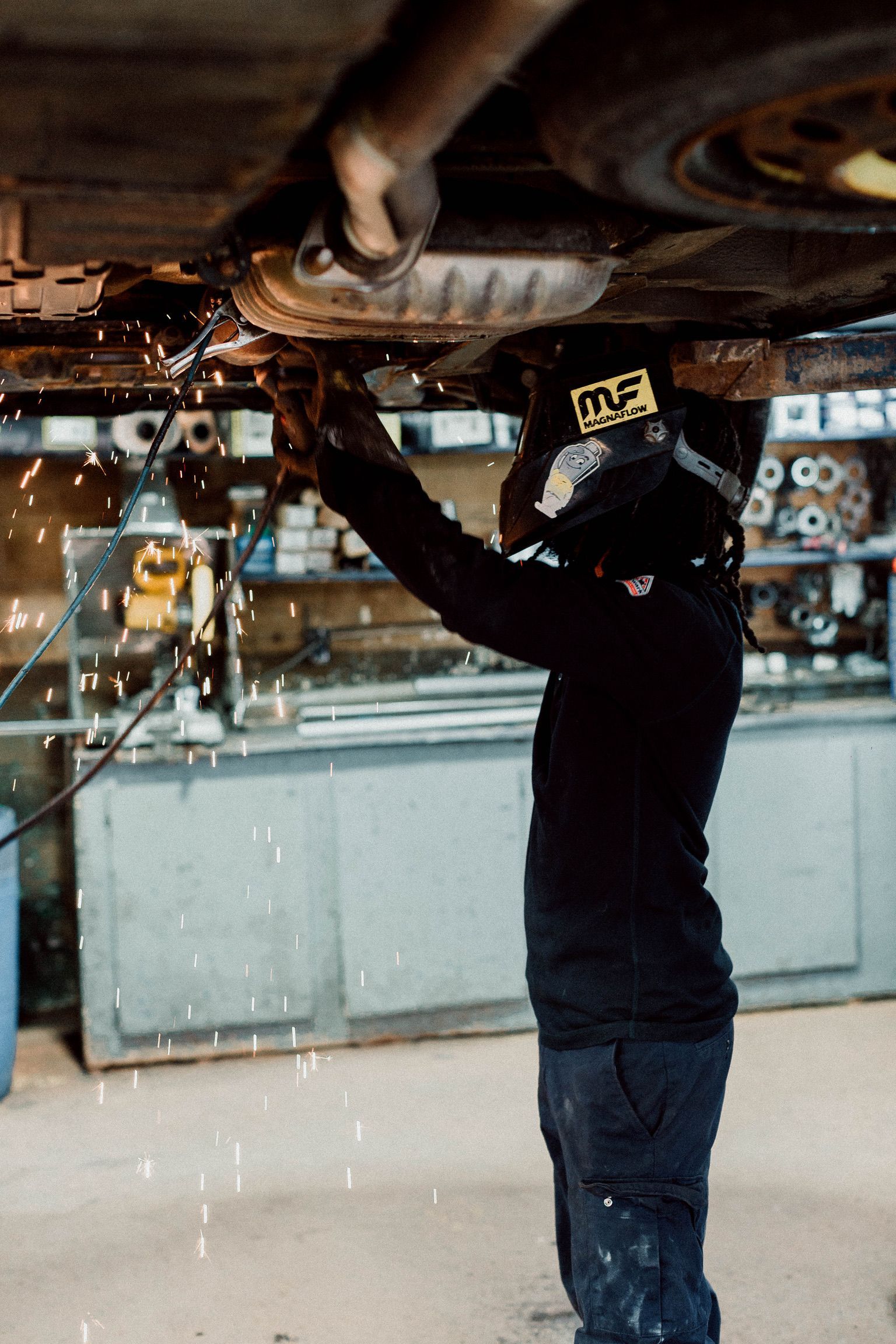 Un homme portant un casque de soudage travaille sous une voiture.