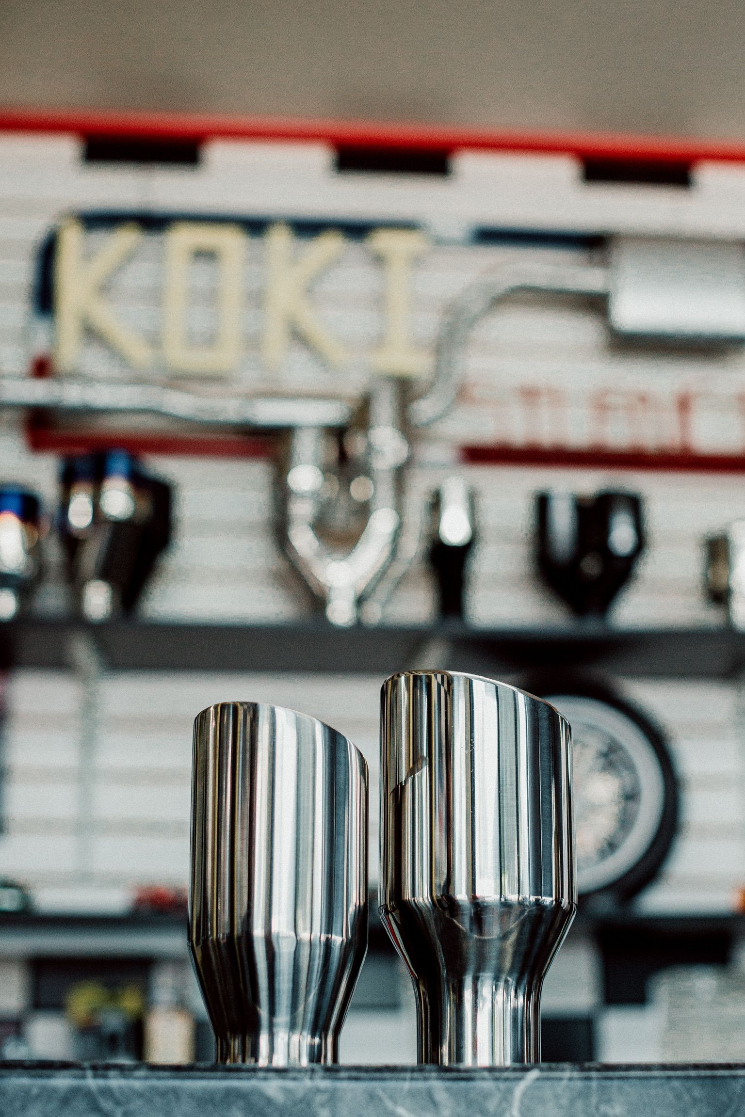 Deux tasses en acier inoxydable sont posées sur un comptoir devant un panneau indiquant koki.