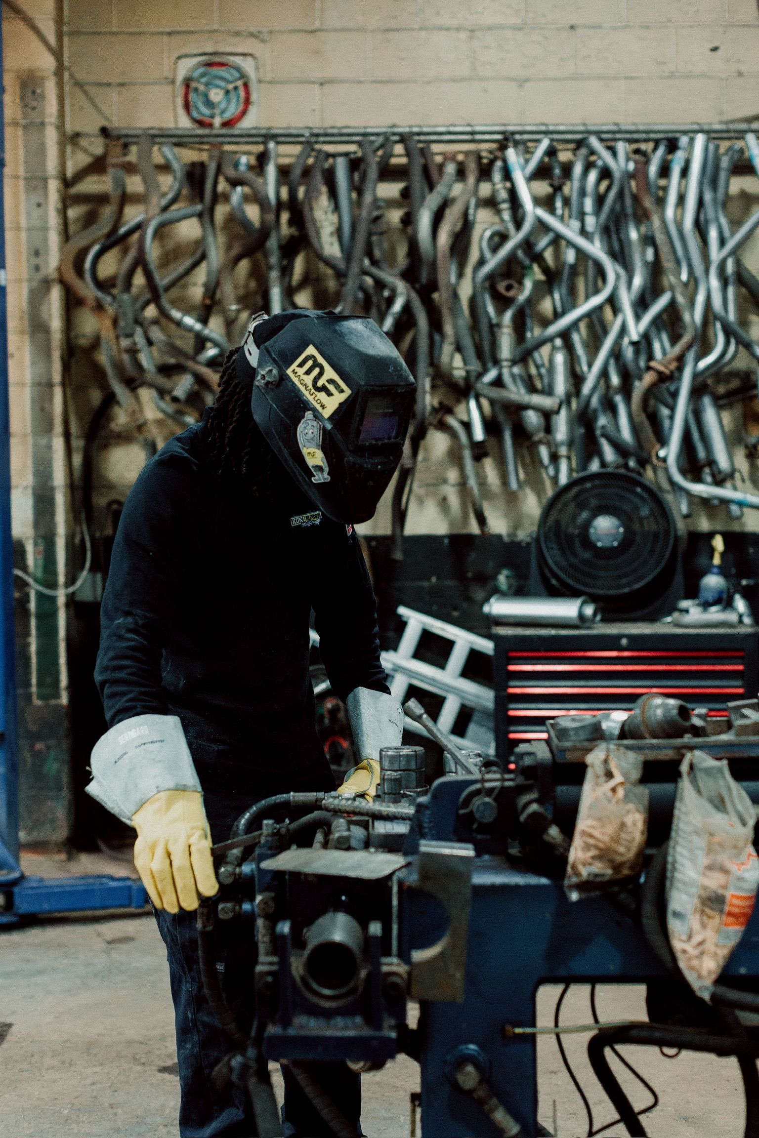 Un homme portant un casque de soudage travaille sur une machine dans un garage.