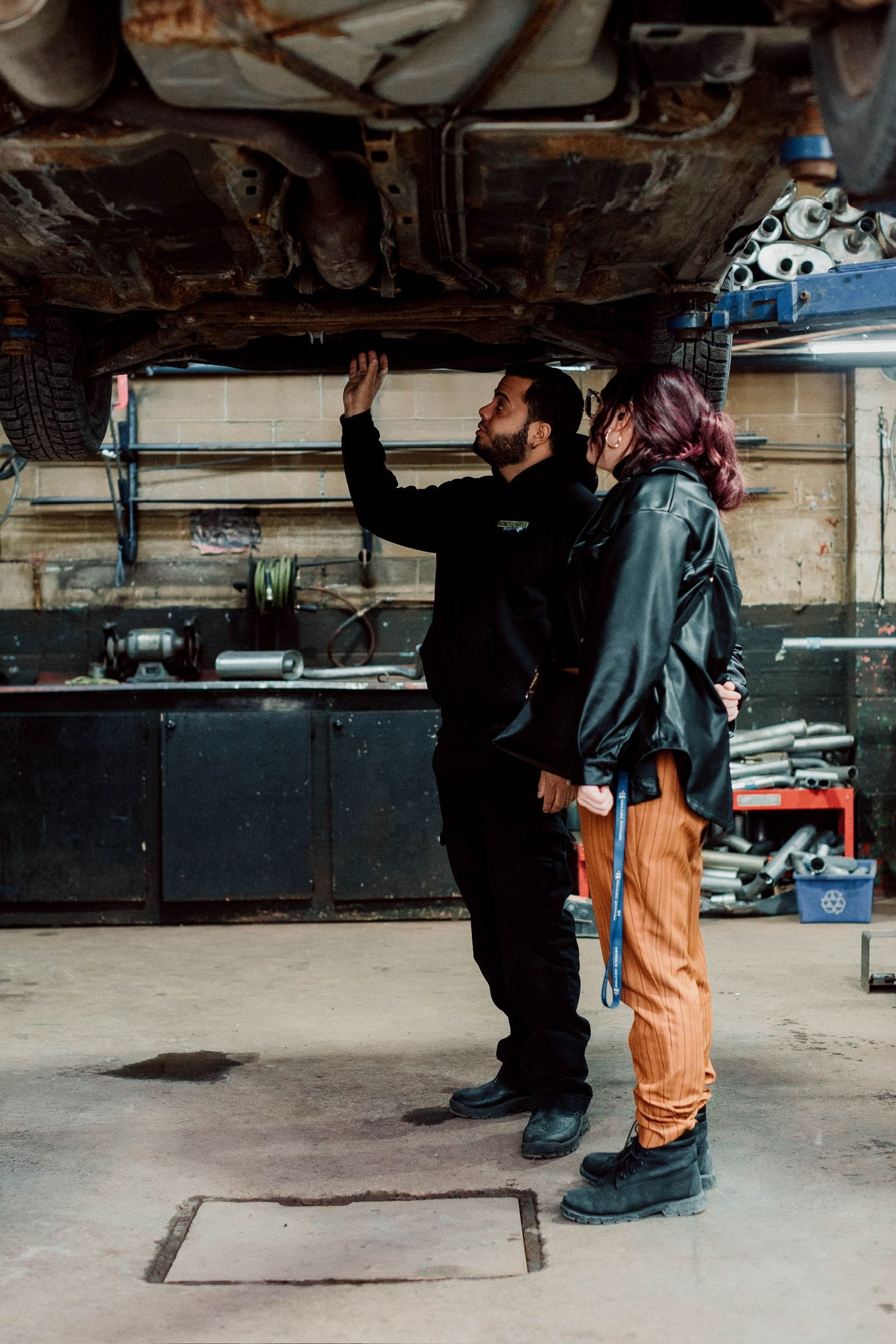 Un homme et une femme regardent sous une voiture dans un garage.