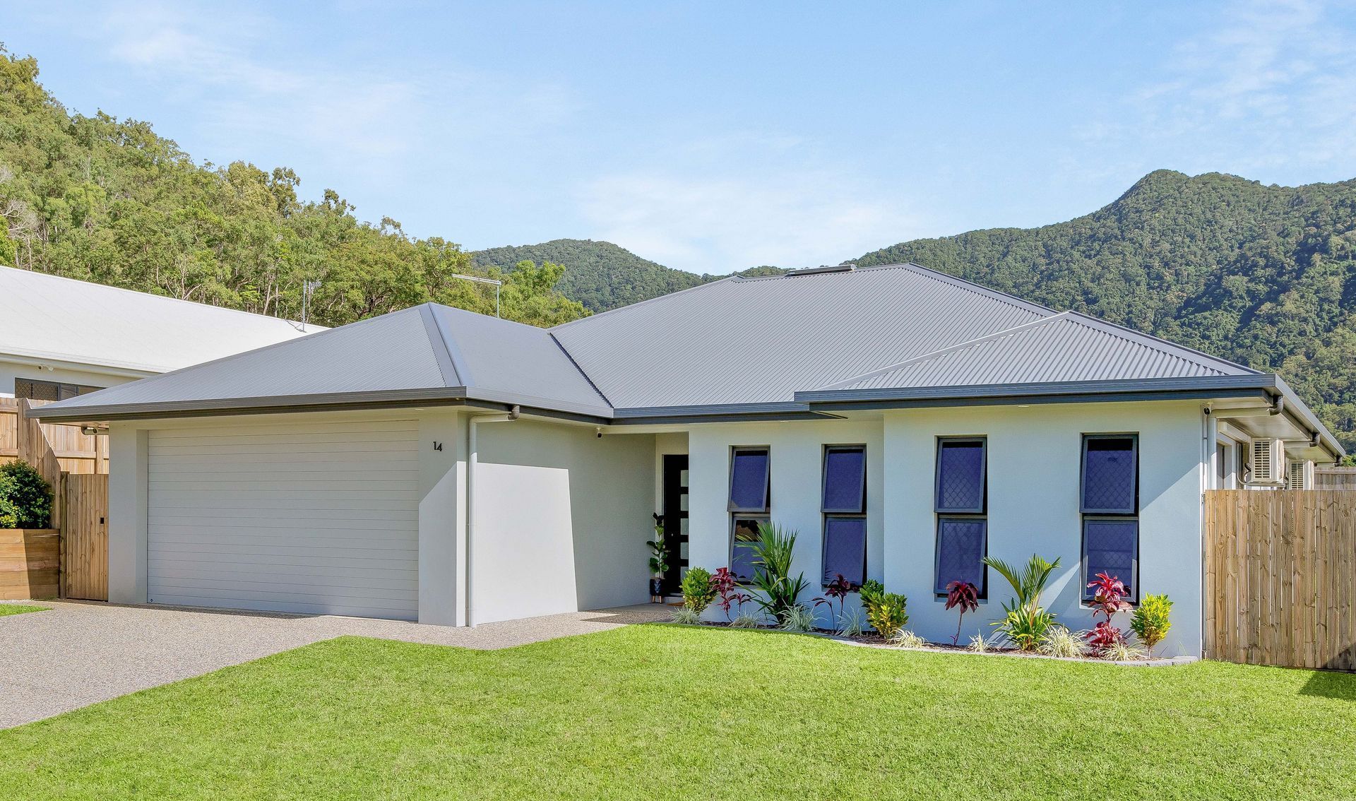 A White House With a Gray Roof is Sitting on Top of a Lush Green Hillside — Ashlee Jones Homes in Gordonvale, QLD