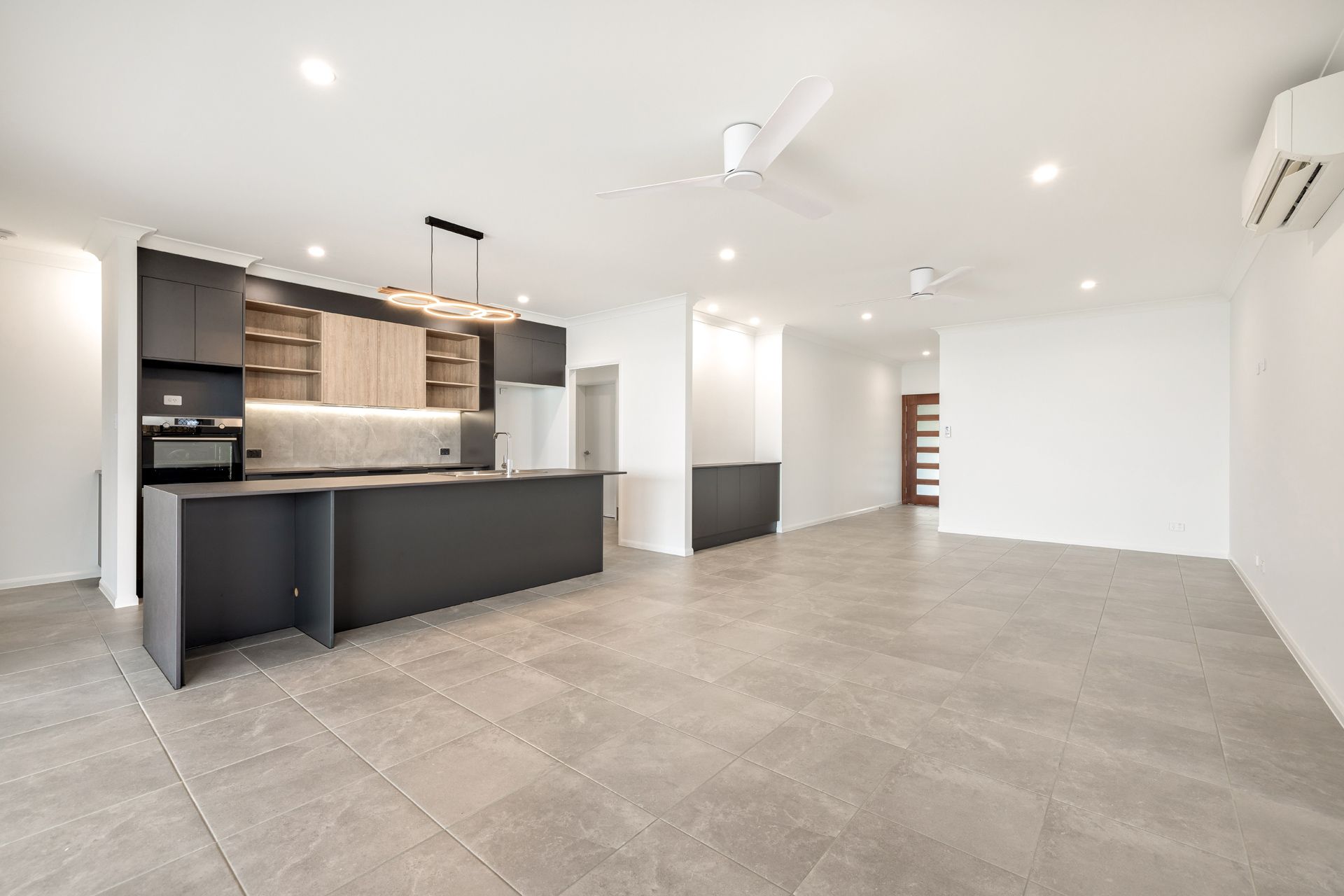 An Open-plan Kitchen and Living Space With Grey Tiled Flooring, Dark Cabinets — Ashlee Jones Homes in Gordonvale, QLD
