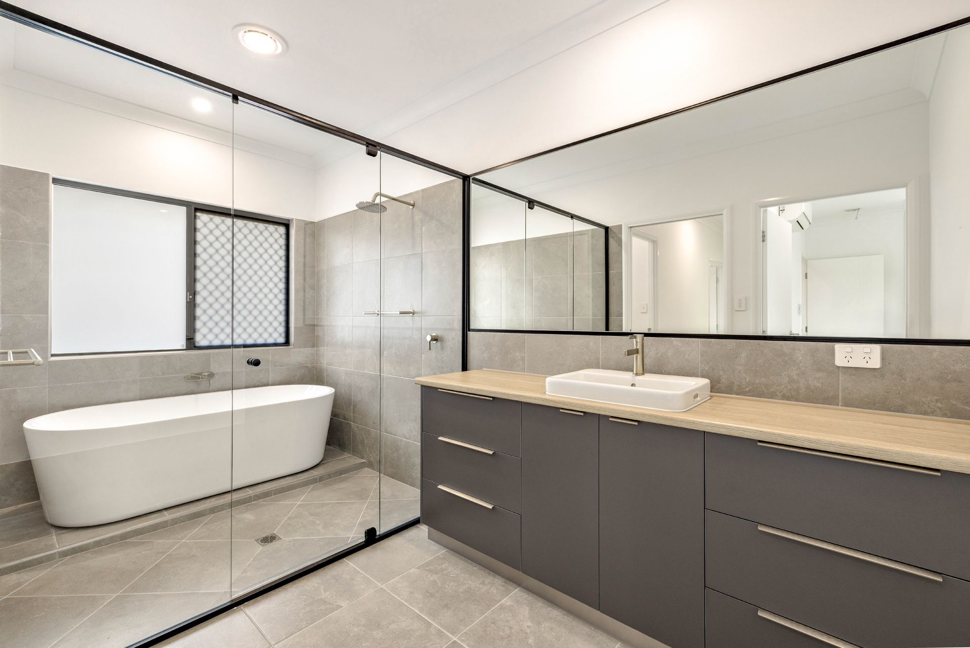 Modern Bathroom With a Freestanding White Tub, Grey Tile Flooring — Ashlee Jones Homes in Gordonvale, QLD