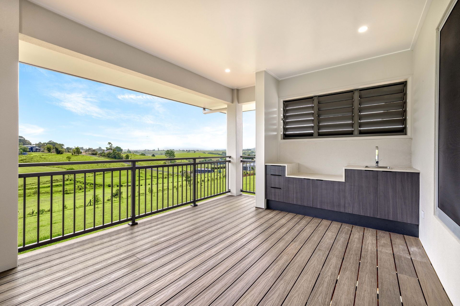 A Covered Balcony With Wooden Decking, a Dark-toned Outdoor Kitchen — Ashlee Jones Homes in Gordonvale, QLD