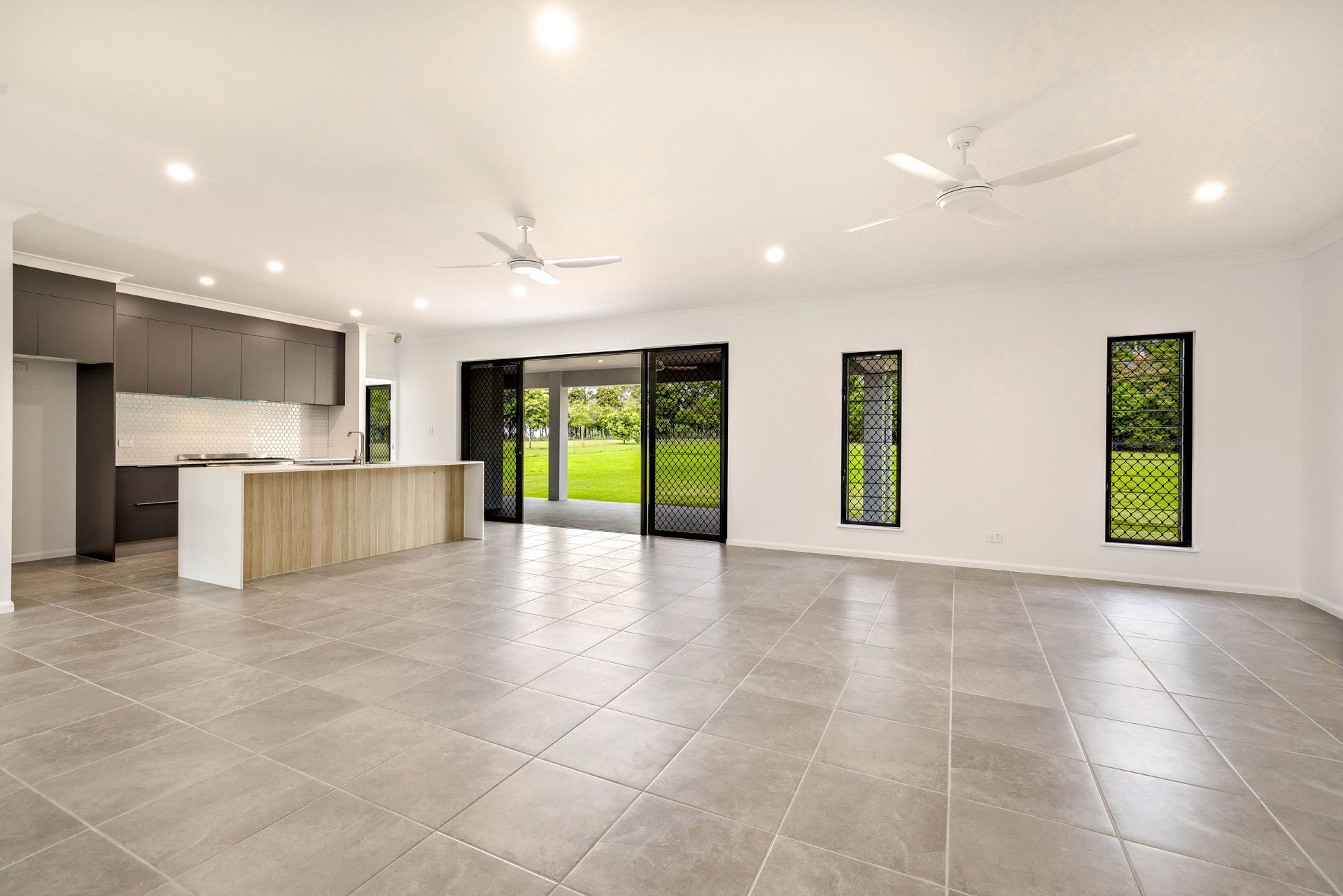 A Modern, Spacious, Open-plan Kitchen and Living Area With Grey Tiled Floors — Ashlee Jones Homes in Gordonvale, QLD