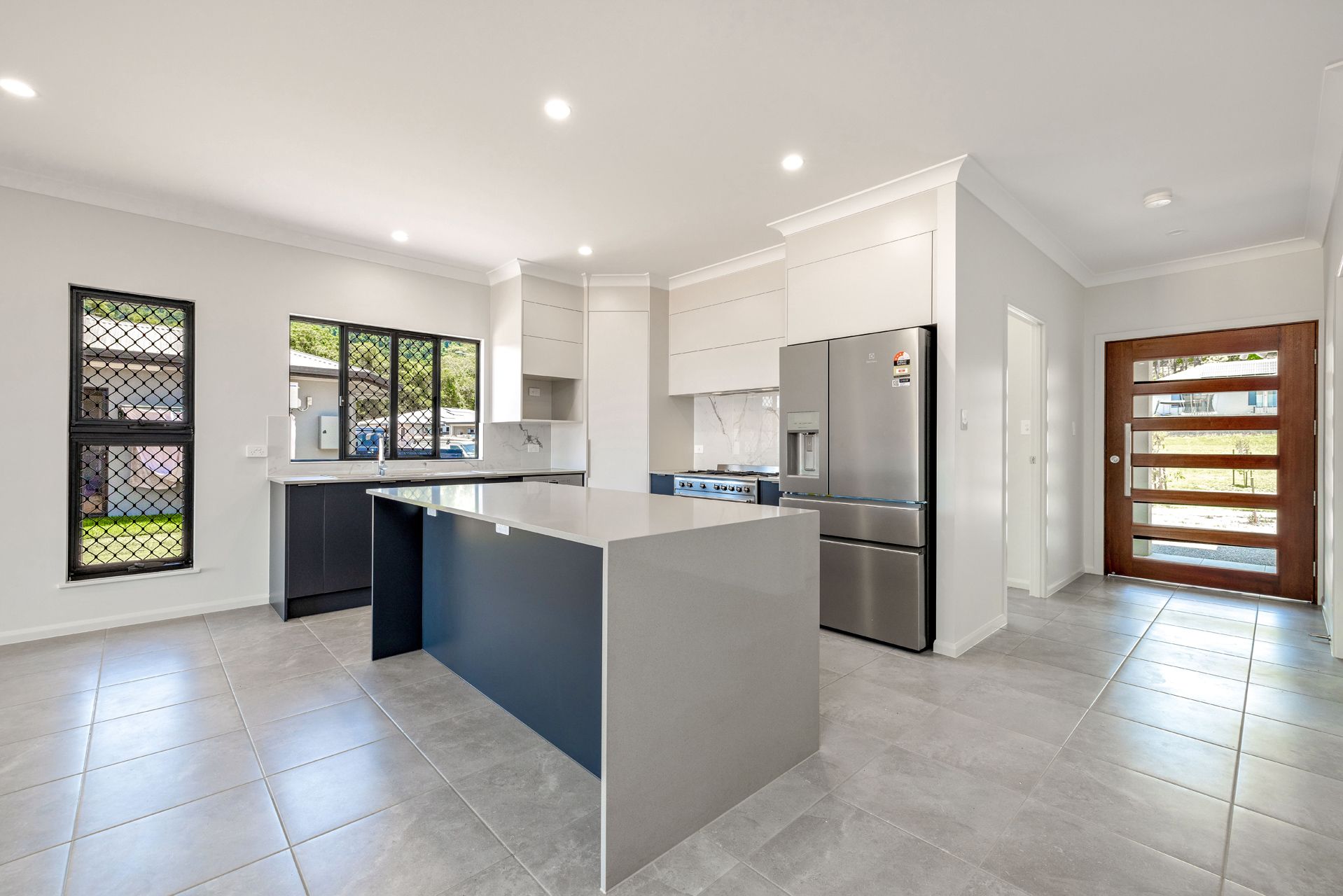 Modern Kitchen Featuring a Grey Island, Stainless Steel Refrigerator — Ashlee Jones Homes in Gordonvale, QLD