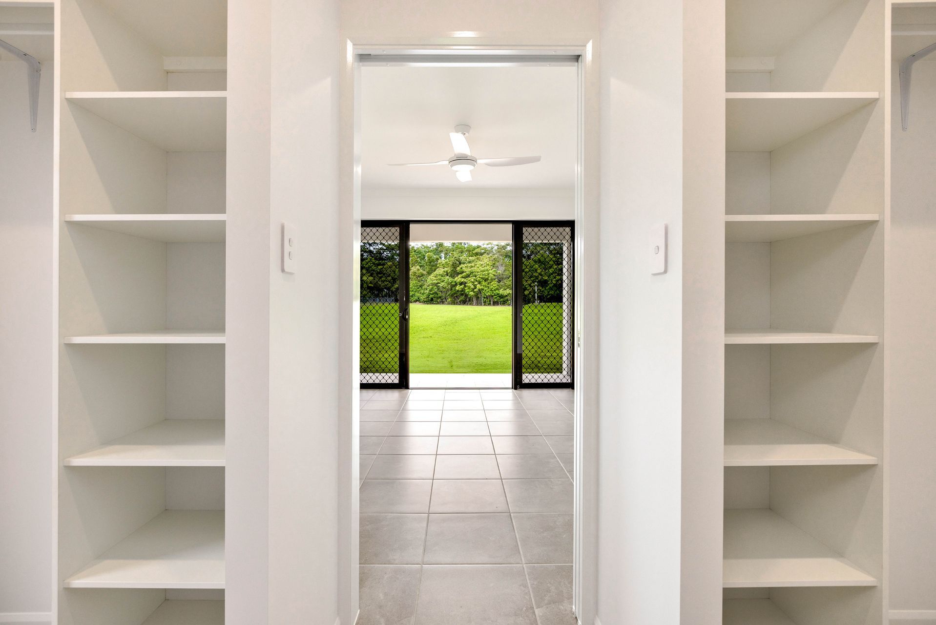 A Walk-in Closet With White Open Shelving on Both Sides Leading — Ashlee Jones Homes in Gordonvale, QLD