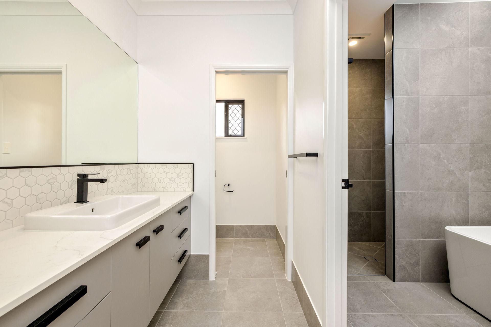 Modern Bathroom Featuring a Light Gray Vanity With a Matte Black Faucet — Ashlee Jones Homes in Gordonvale, QLD
