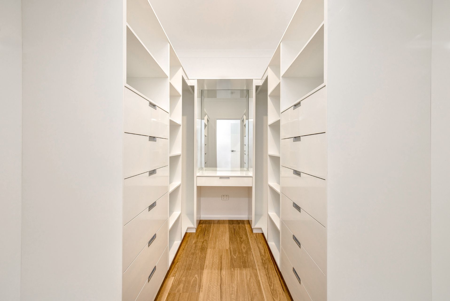 A Minimalist Walk-in Closet Featuring Floor-to-ceiling White Cabinetry — Ashlee Jones Homes in Gordonvale, QLD