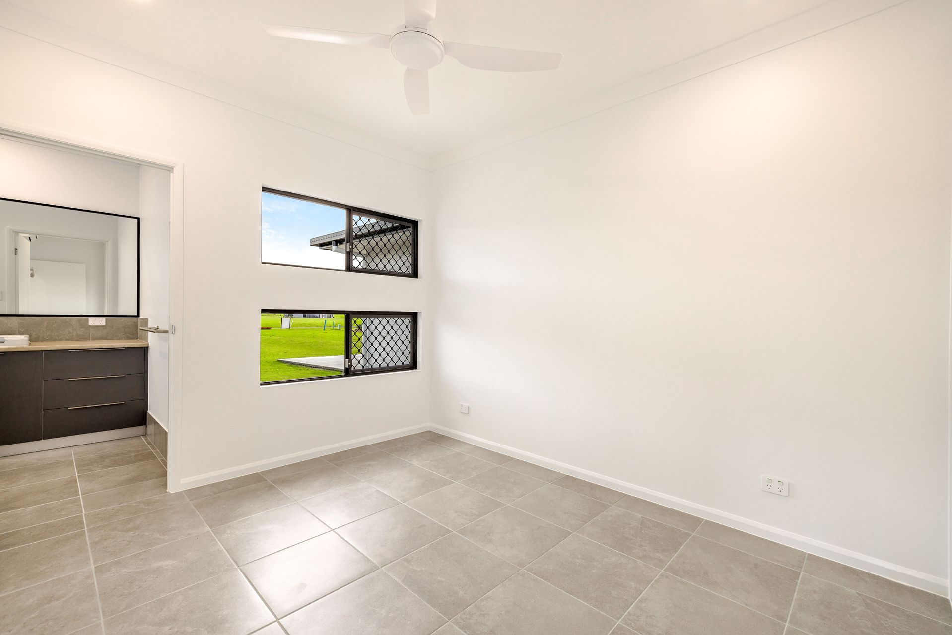 A Bright, Empty Bedroom With White Walls, Grey Tile Flooring — Ashlee Jones Homes in Gordonvale, QLD
