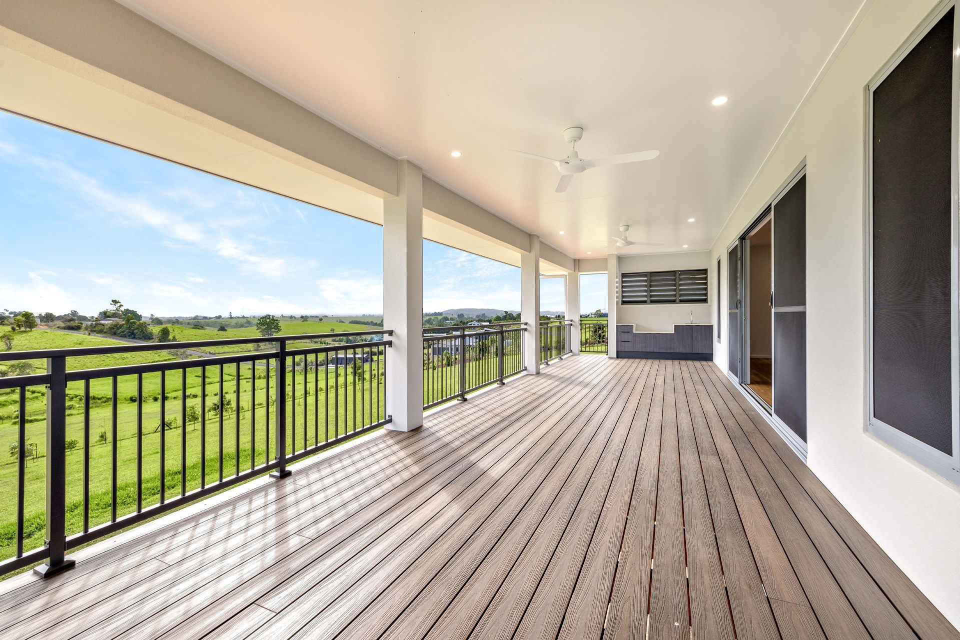 A Wide, Covered Balcony With Wooden Decking and Black Railings — Ashlee Jones Homes in Gordonvale, QLD