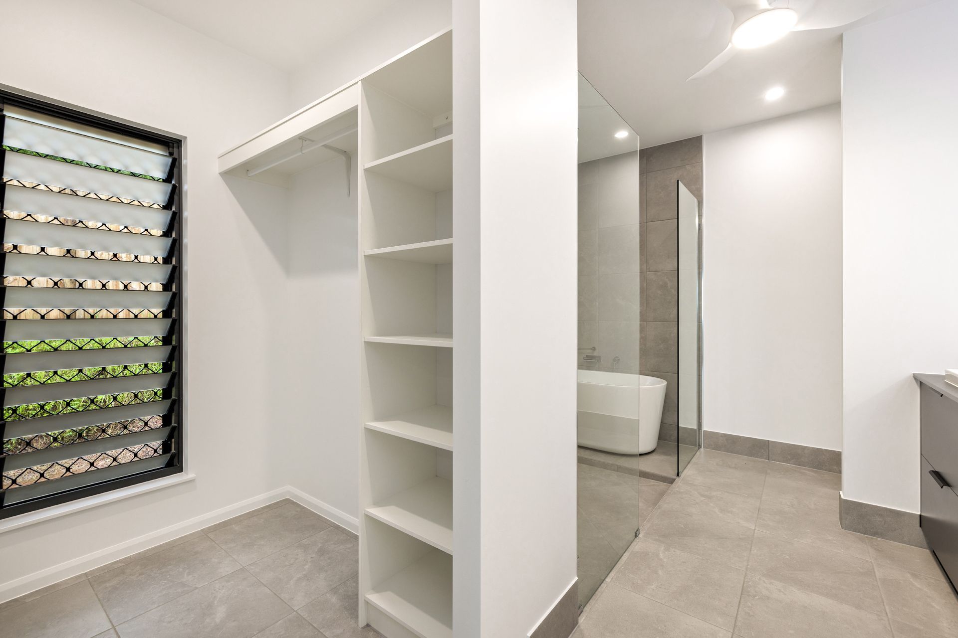 A Walk-in Wardrobe With White Shelving and Grey Tile Flooring — Ashlee Jones Homes in Gordonvale, QLD
