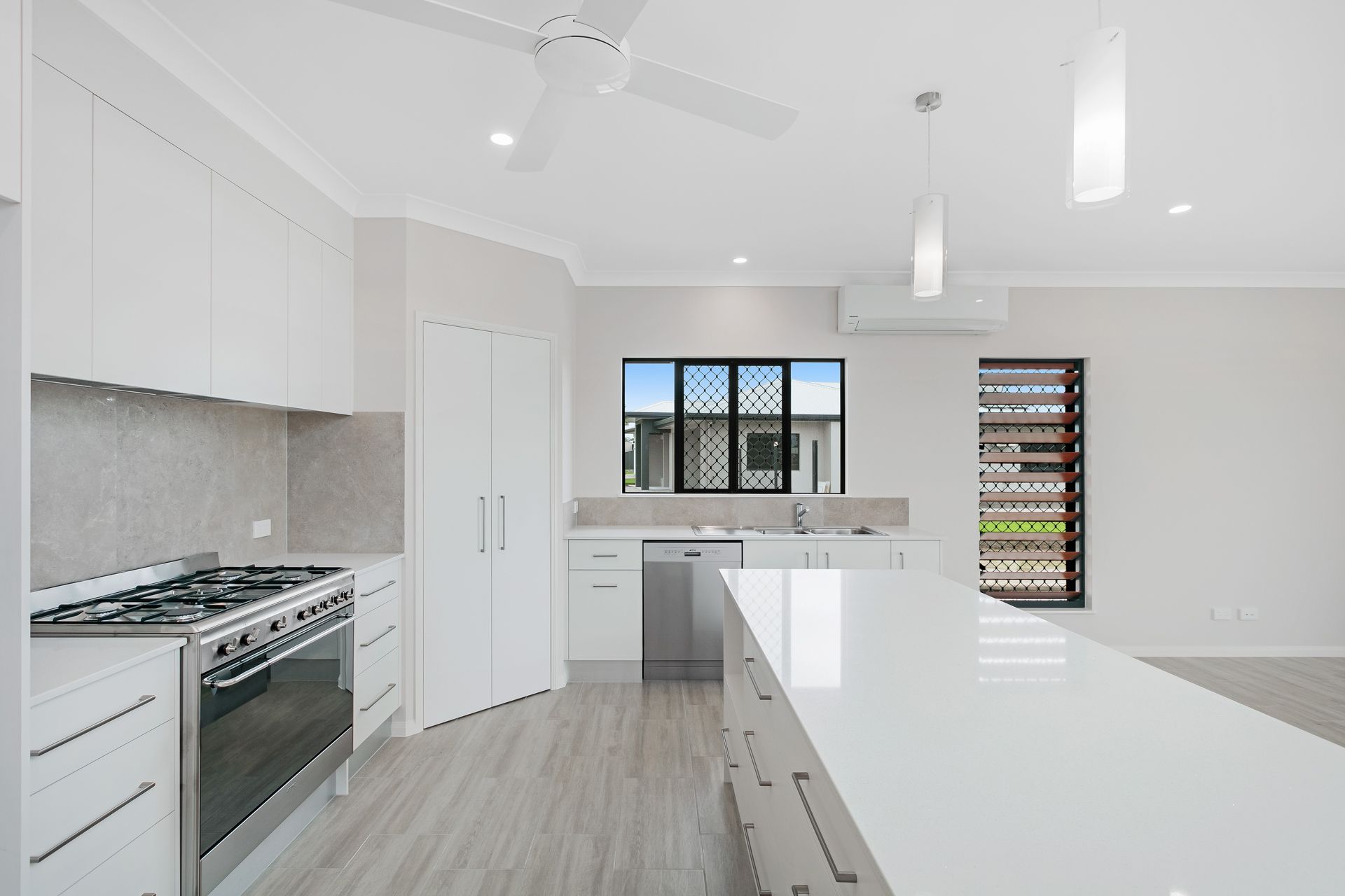 A Modern, Minimalist Kitchen With White Cabinets, a Large Island — Ashlee Jones Homes in Gordonvale, QLD