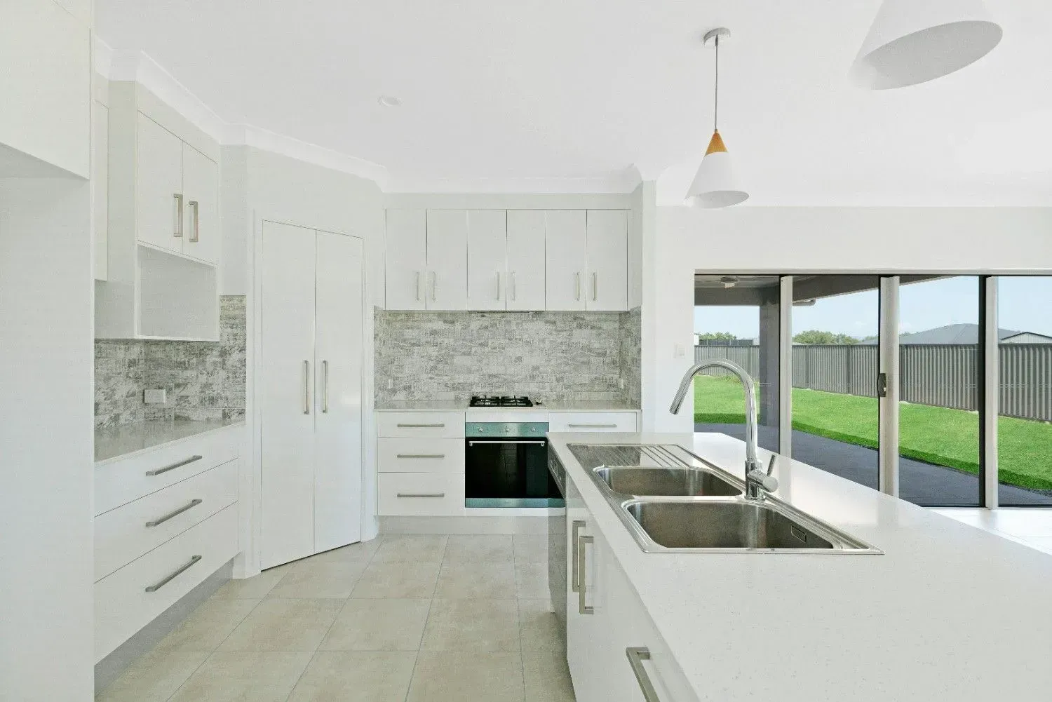 A White House With a Brown Garage Door is Sitting on Top of a Lush Green Lawn — Ashlee Jones Homes in Gordonvale, QLD