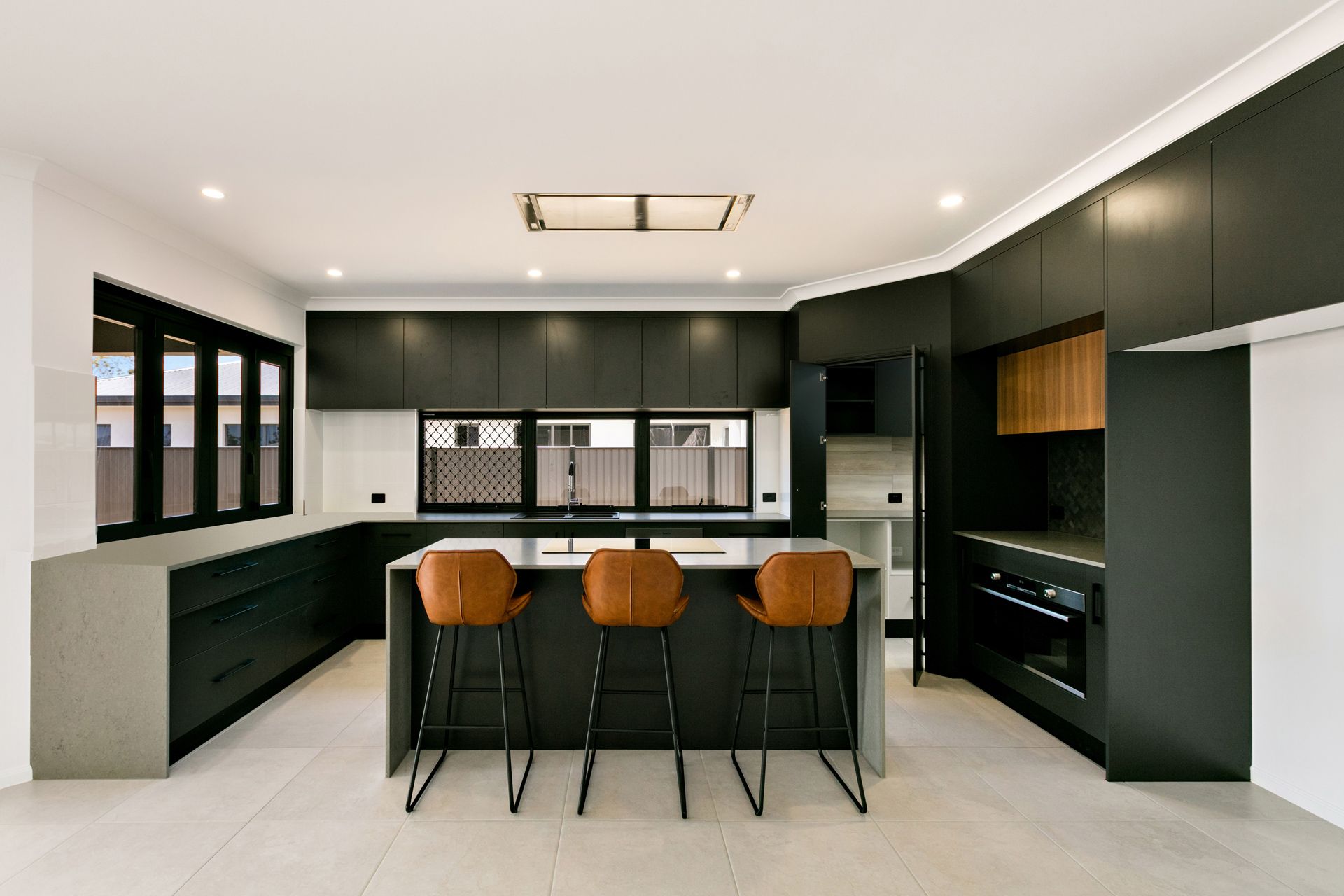 A Modern, Minimalist Kitchen Featuring Dark Cabinetry, a Central Island — Ashlee Jones Homes in Gordonvale, QLD