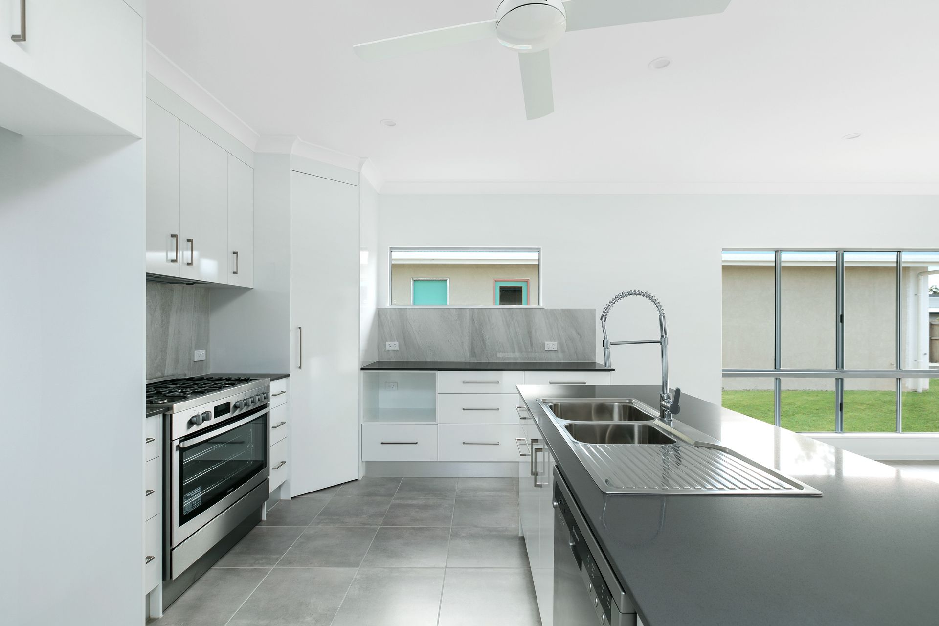 A Modern, White Kitchen Featuring a Large Island With a Stainless Steel Sink — Ashlee Jones Homes in Gordonvale, QLD