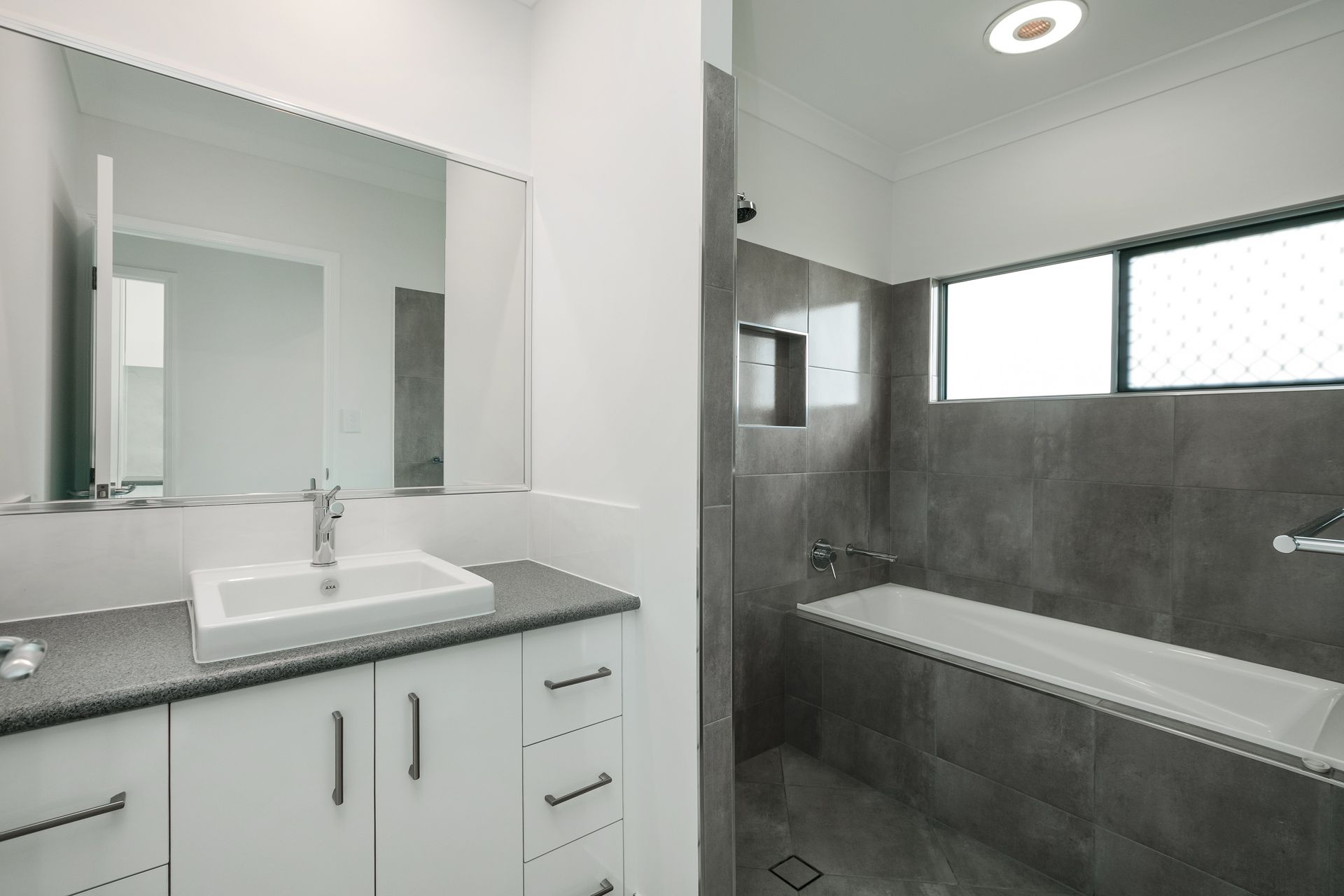 A Modern Bathroom With a White Vanity, a Large Mirror — Ashlee Jones Homes in Gordonvale, QLD