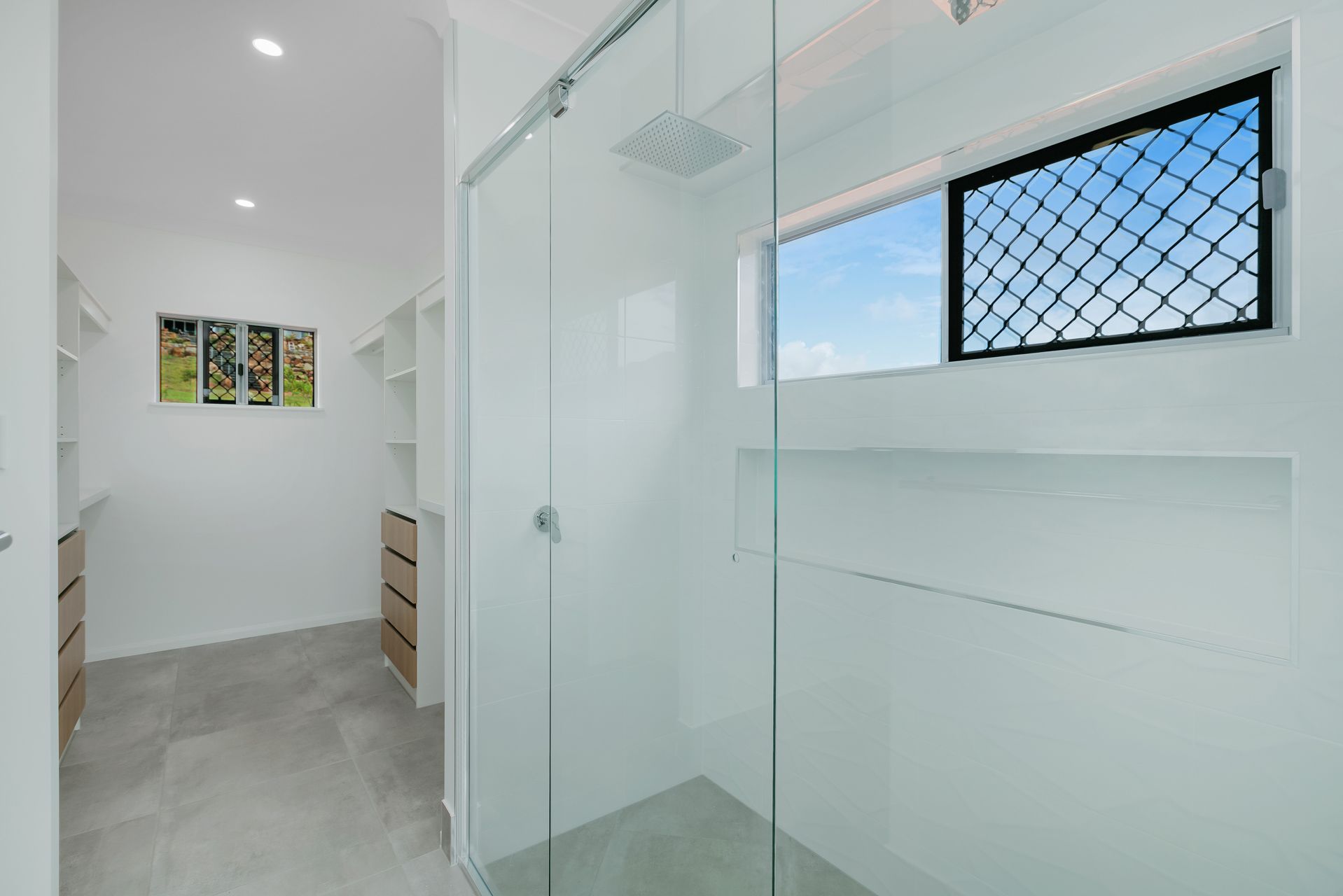 A Minimalist Walk-in Closet Flows Into a Glass-enclosed Shower — Ashlee Jones Homes in Gordonvale, QLD