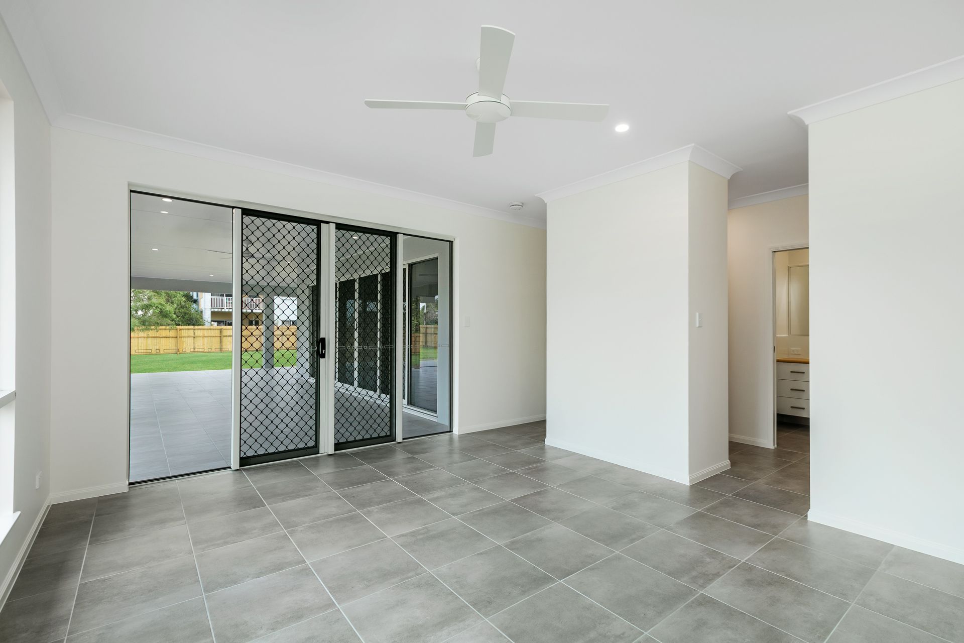 An Empty Living Area With Grey Tiled Flooring, a Ceiling Fan — Ashlee Jones Homes in Gordonvale, QLD