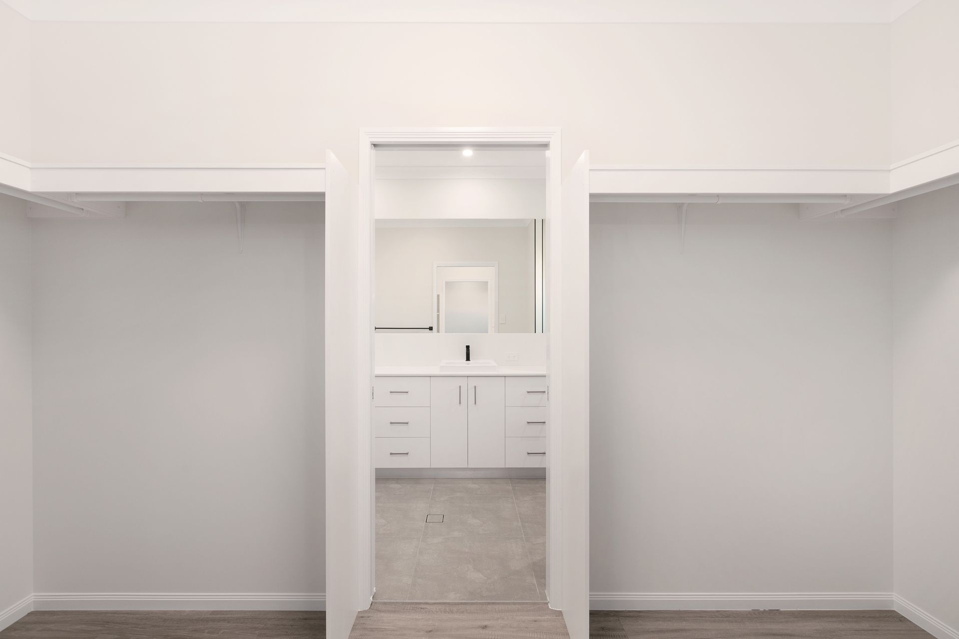 An Empty, Minimalist Walk-in Closet With White Walls Leading to a Bright — Ashlee Jones Homes in Gordonvale, QLD