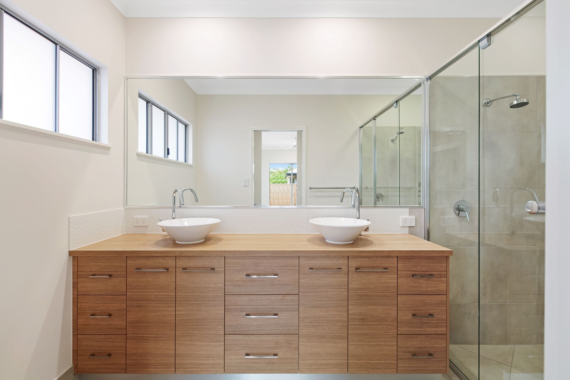 Modern Bathroom Featuring a Wood Vanity With Two White Vessel Sinks — Ashlee Jones Homes in Gordonvale, QLD