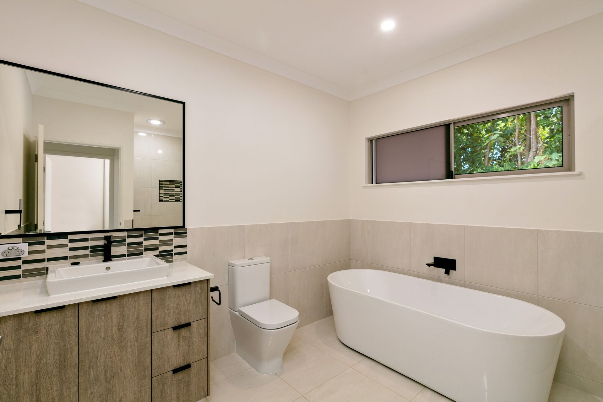 A Modern Bathroom Featuring a Wood-toned Vanity — Ashlee Jones Homes in Gordonvale, QLD