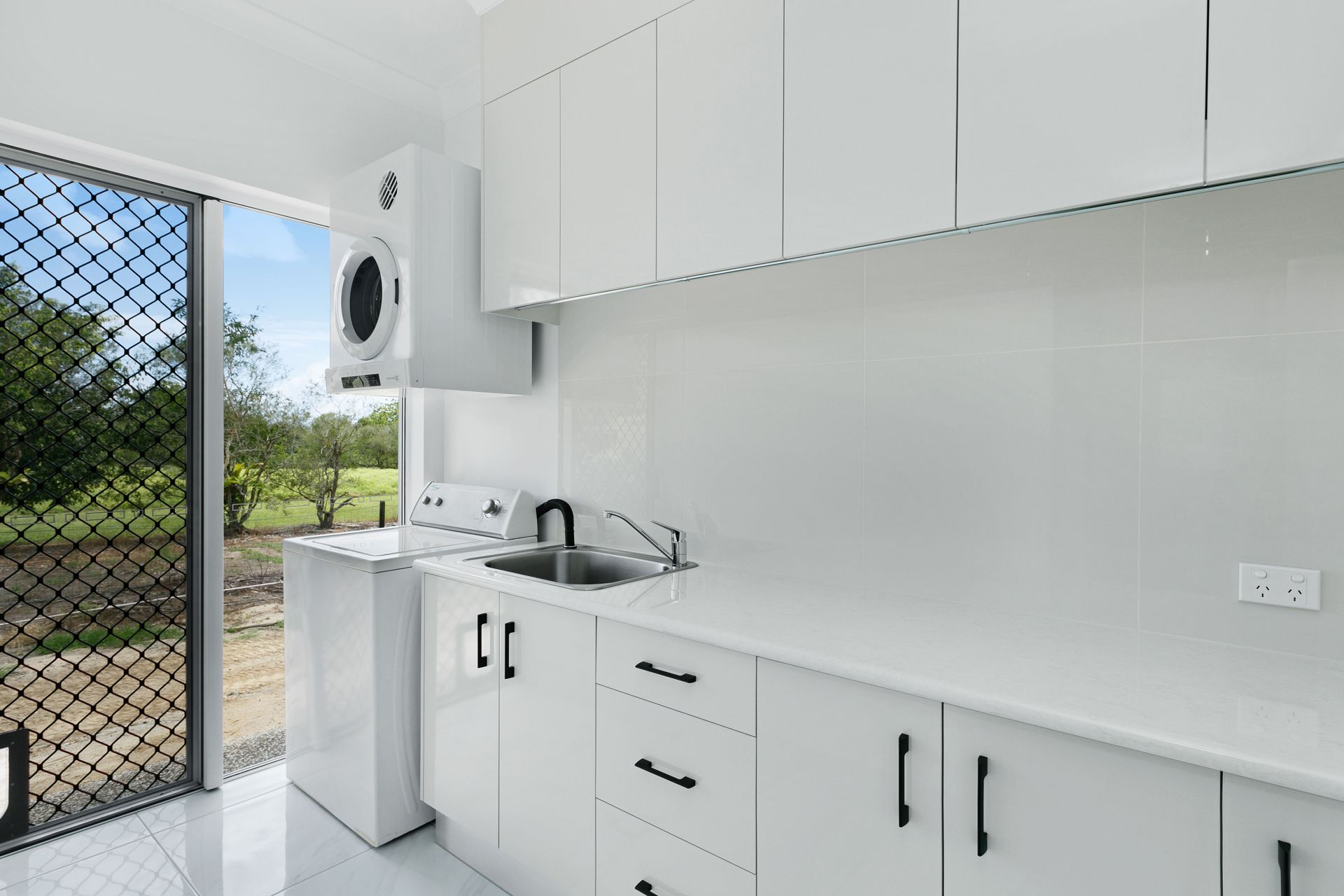 A Modern Laundry Room With White Cabinets, a Matching Countertop — Ashlee Jones Homes in Gordonvale, QLD