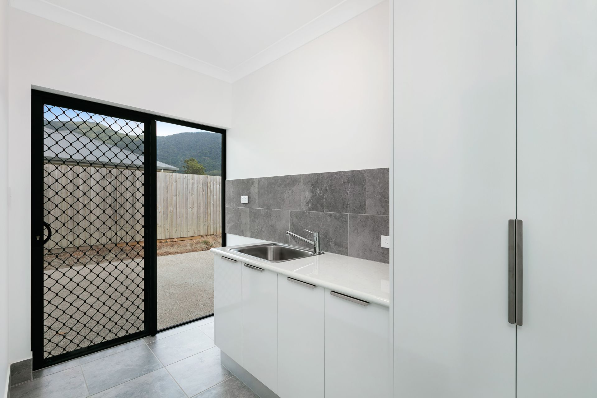 A White Minimalist Kitchen Area With a Sink and Grey Tiled Backsplash — Ashlee Jones Homes in Gordonvale, QLD