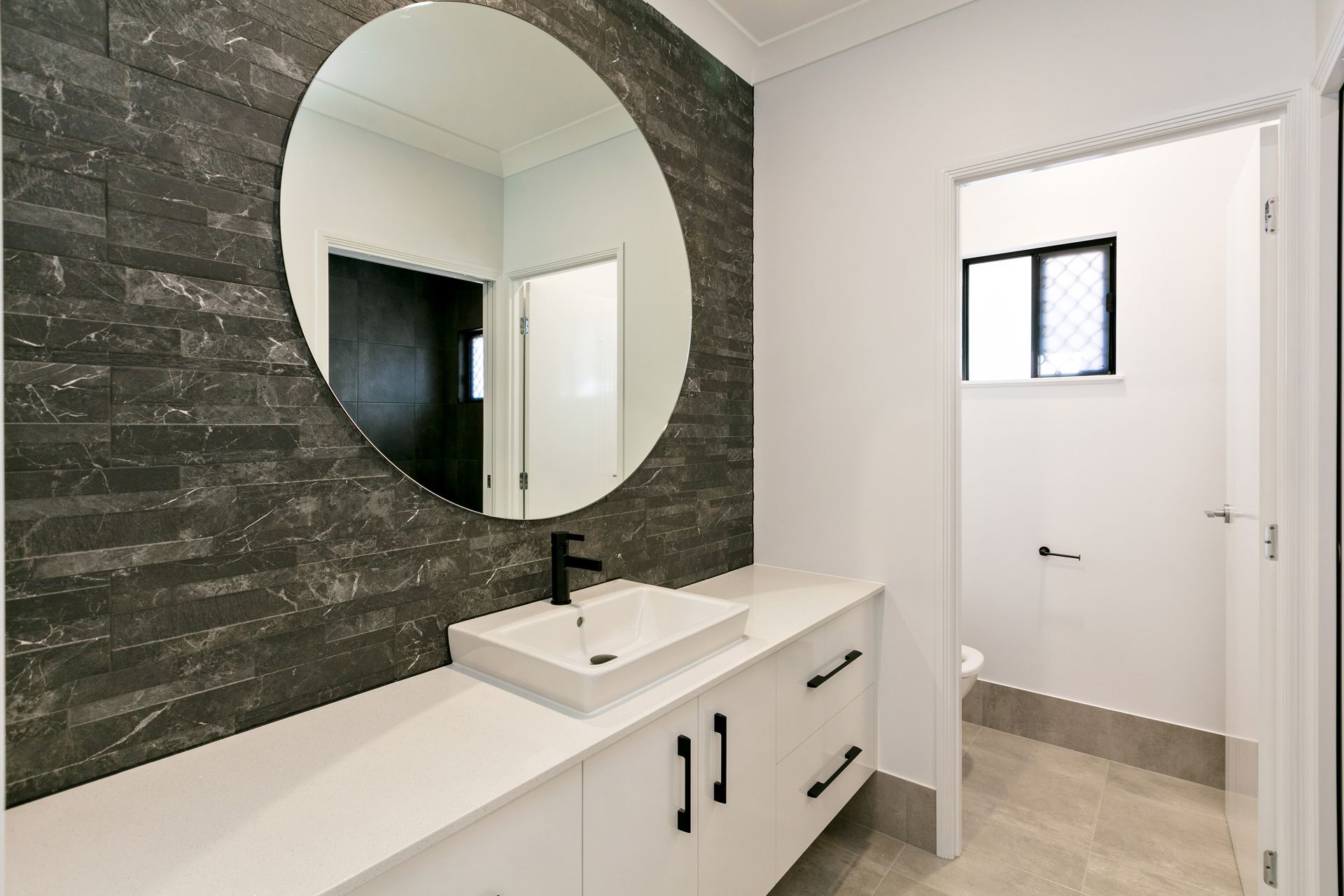 A Modern Bathroom Featuring a White Vanity With a Black Faucet — Ashlee Jones Homes in Gordonvale, QLD