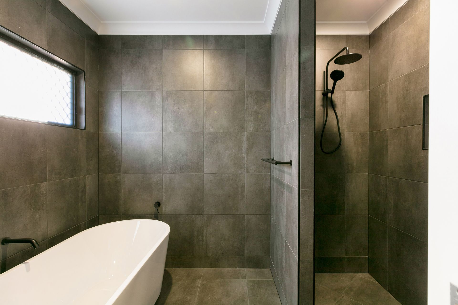 A Modern Bathroom With Dark Grey Tiles, a White Freestanding Bathtub — Ashlee Jones Homes in Gordonvale, QLD
