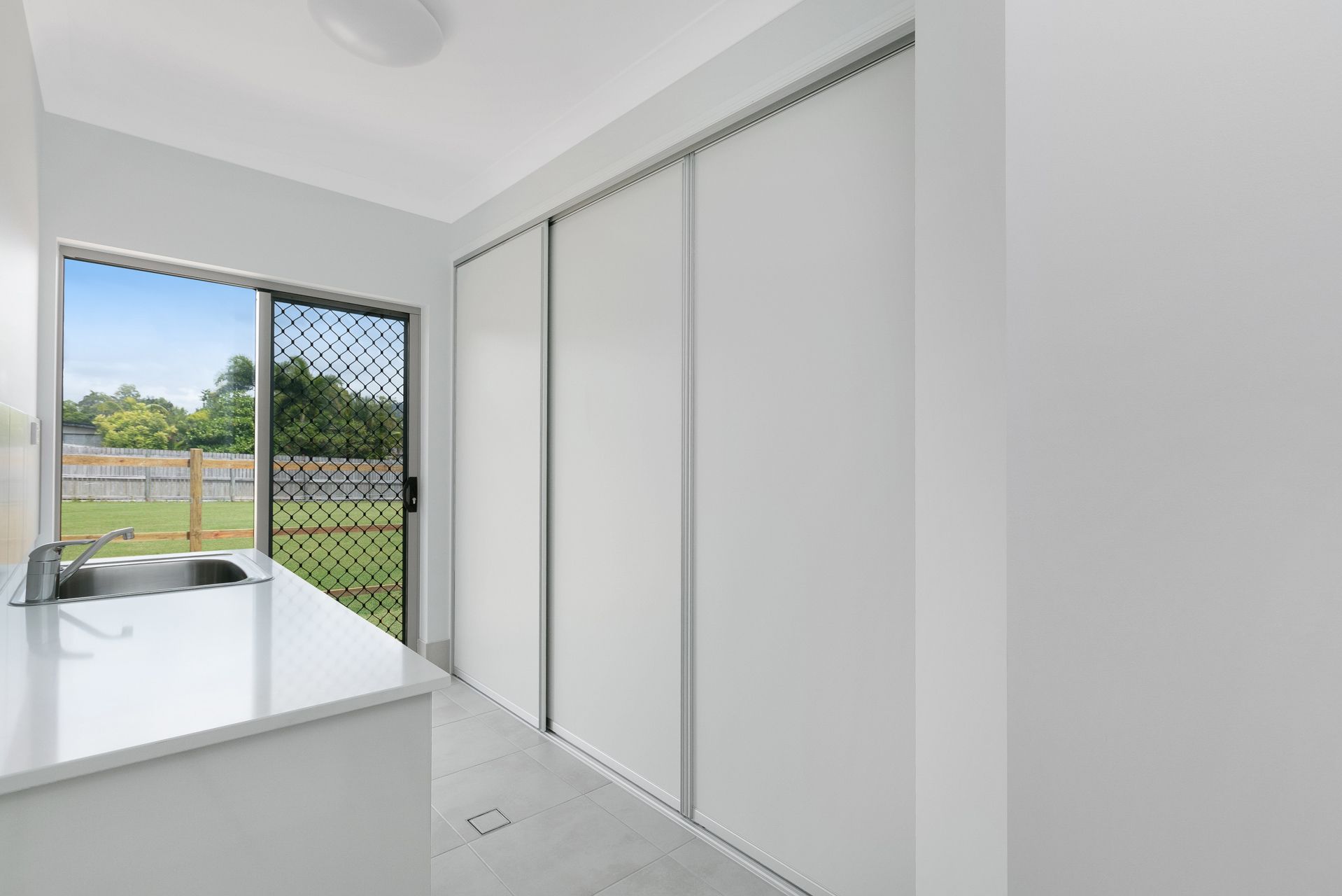 A Bright Laundry Room With White Sliding Cabinet Doors — Ashlee Jones Homes in Gordonvale, QLD