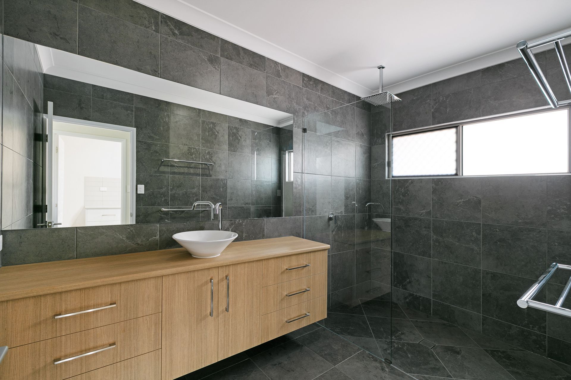 A Modern Bathroom With Dark Grey Stone Walls and Floors — Ashlee Jones Homes in Gordonvale, QLD