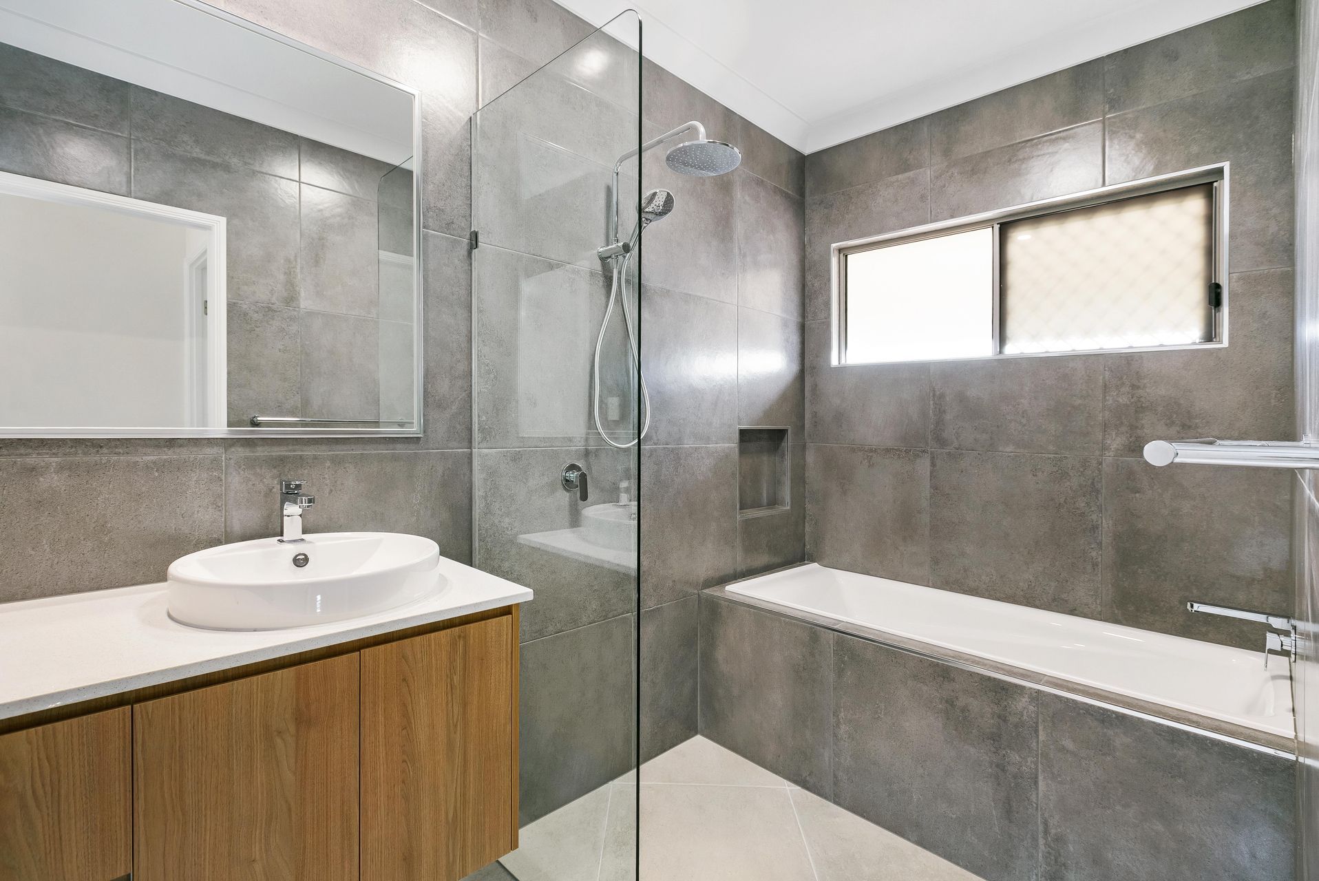 A Modern Bathroom With Grey Tiled Walls, a Wooden Vanity — Ashlee Jones Homes in Gordonvale, QLD