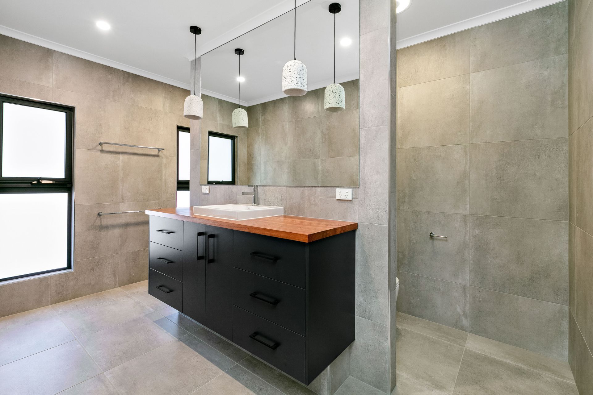 Modern Bathroom With Gray Tiled Walls, a Black Vanity With a Wooden Countertop — Ashlee Jones Homes in Gordonvale, QLD