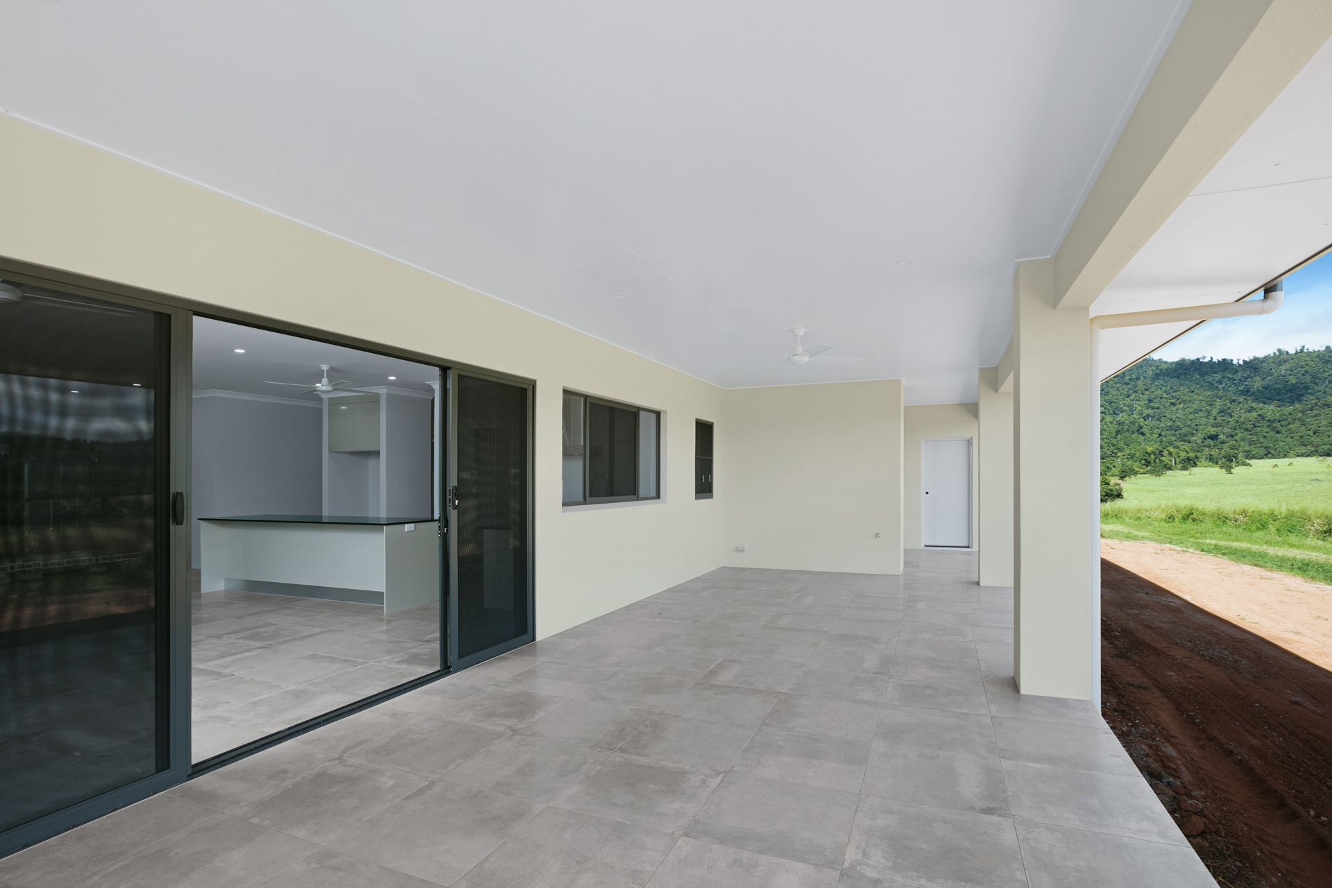 A Modern, Covered Outdoor Patio With Light Grey Tiled Flooring — Ashlee Jones Homes in Gordonvale, QLD