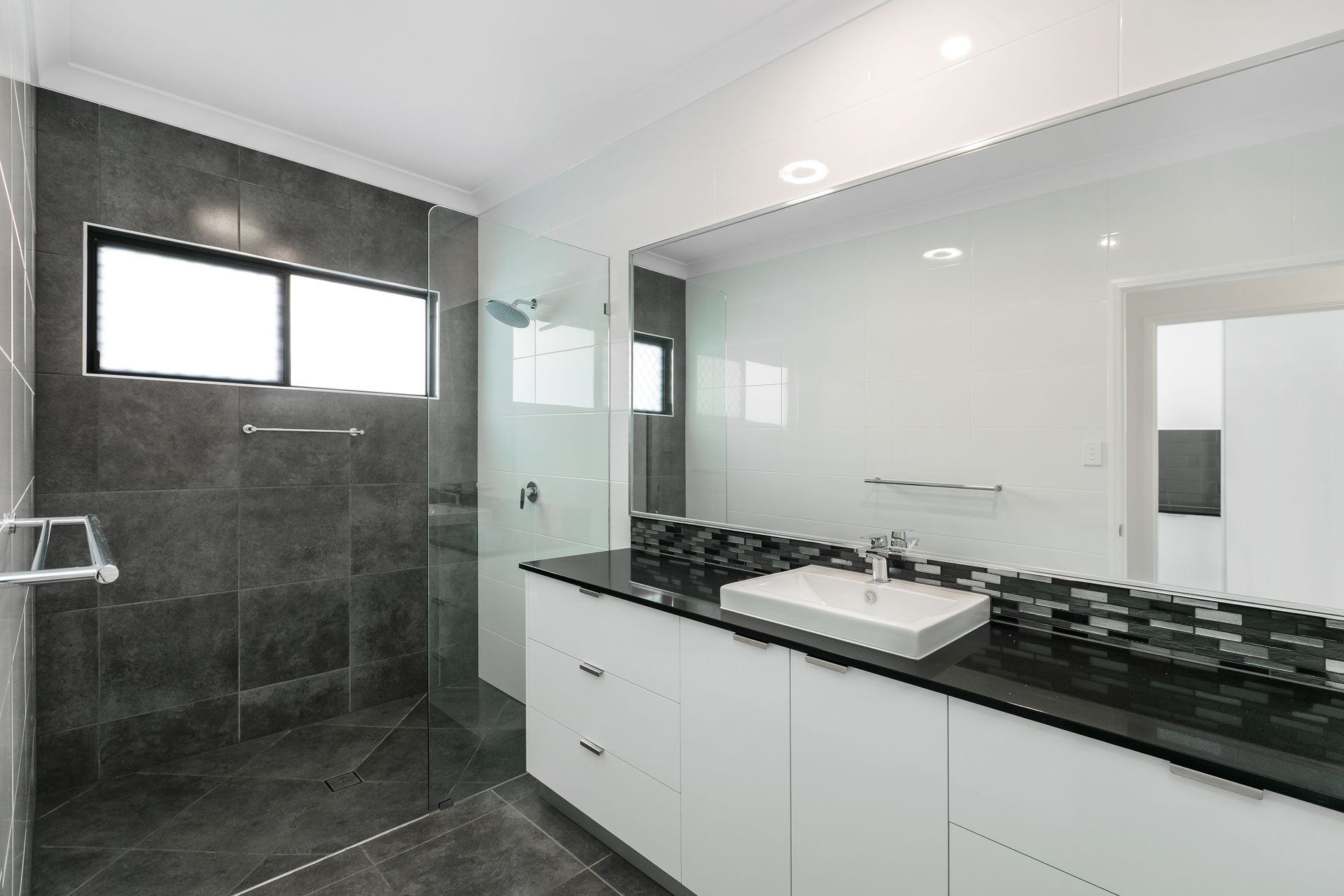A Modern Bathroom Featuring a White Vanity With a Black Countertop — Ashlee Jones Homes in Gordonvale, QLD